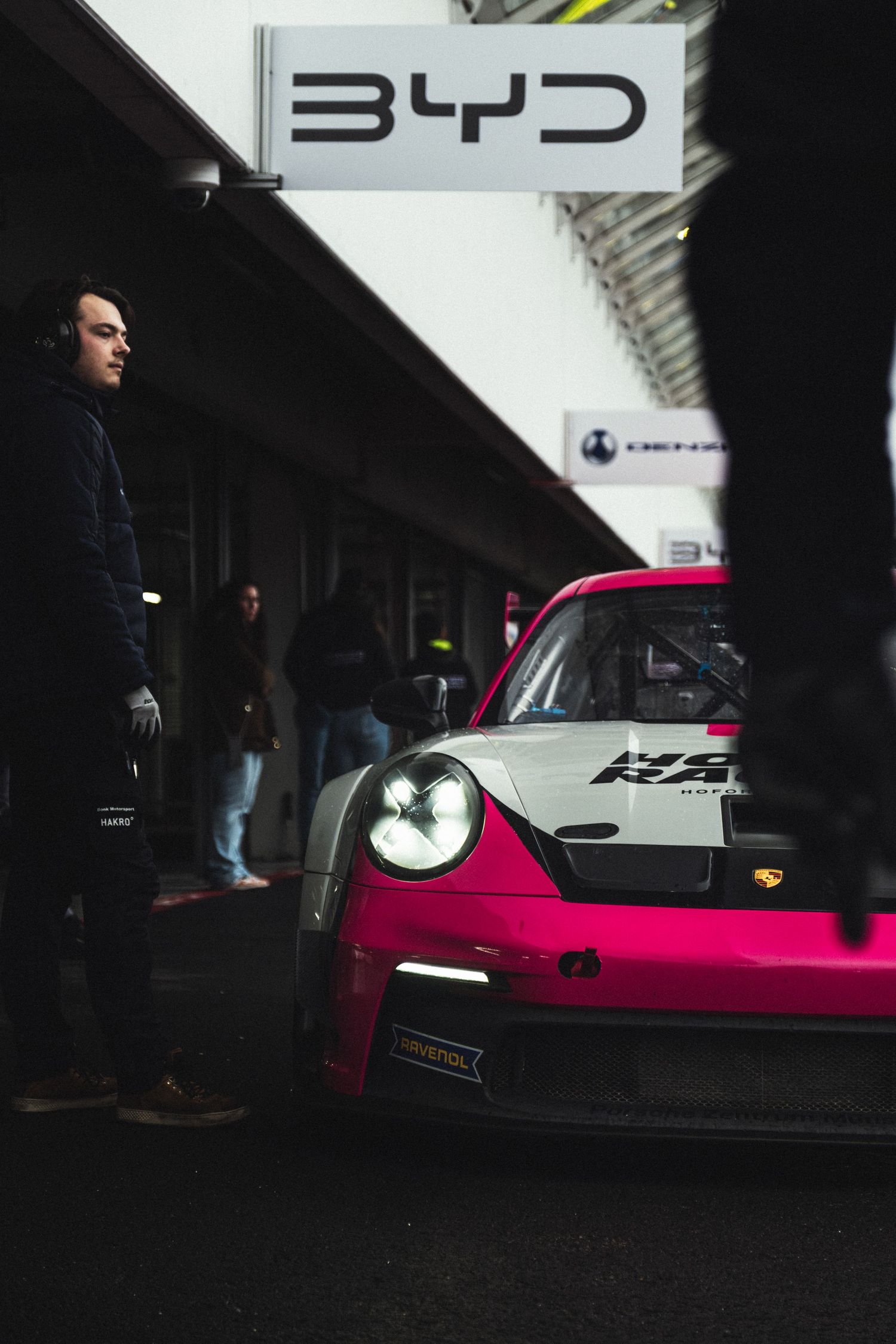 Pink vintage Porsche racing car displayed in a dark garage setting.