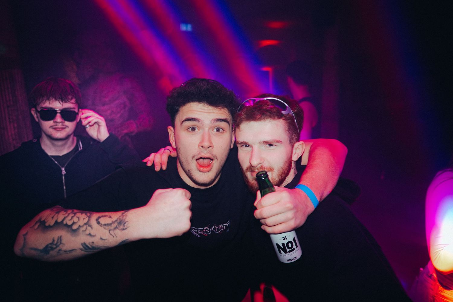 People dancing and enjoying a nightclub party with vibrant purple and red lighting effects.