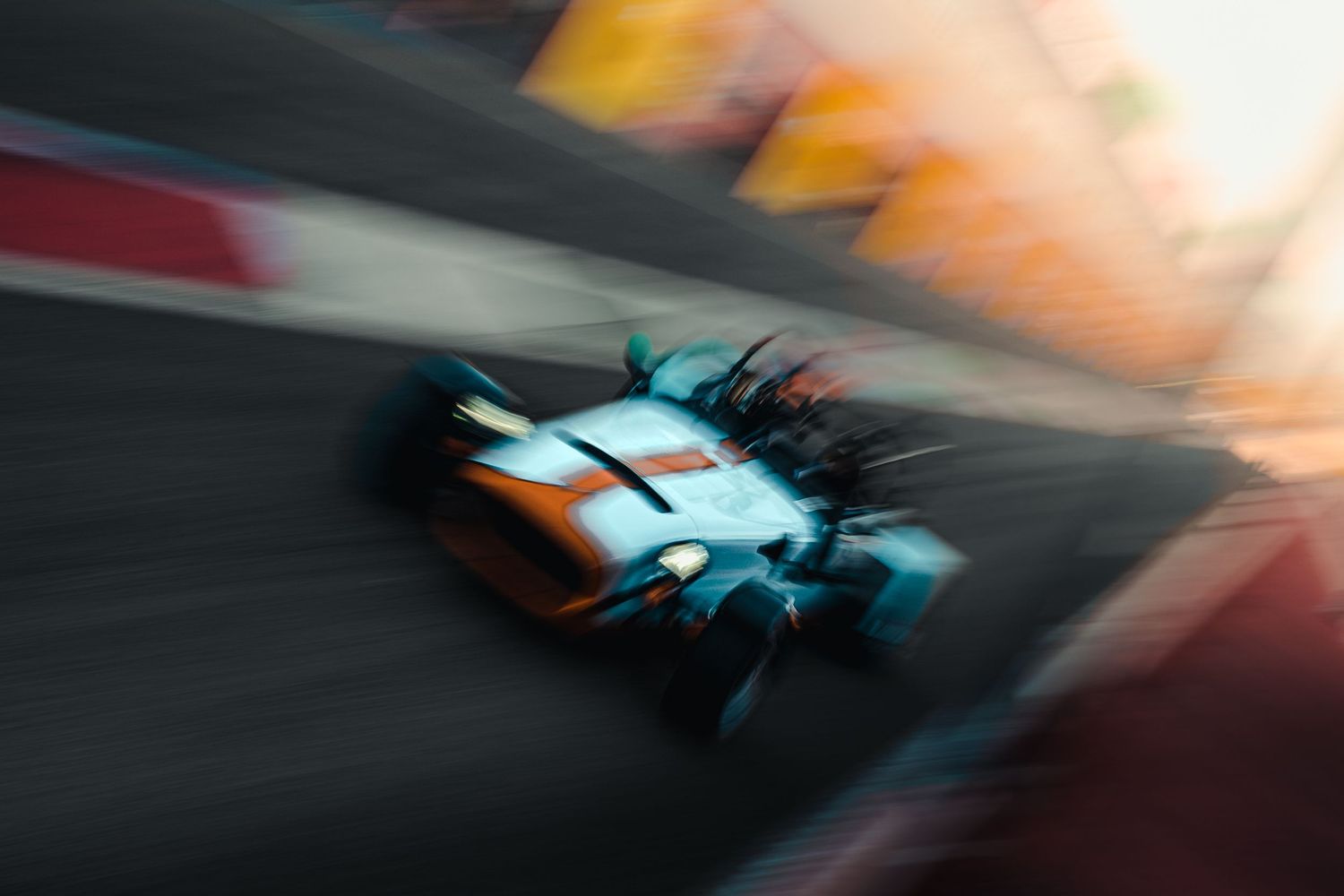 Blurred motion shot of Gulf-liveried open-wheel race car on circuit.