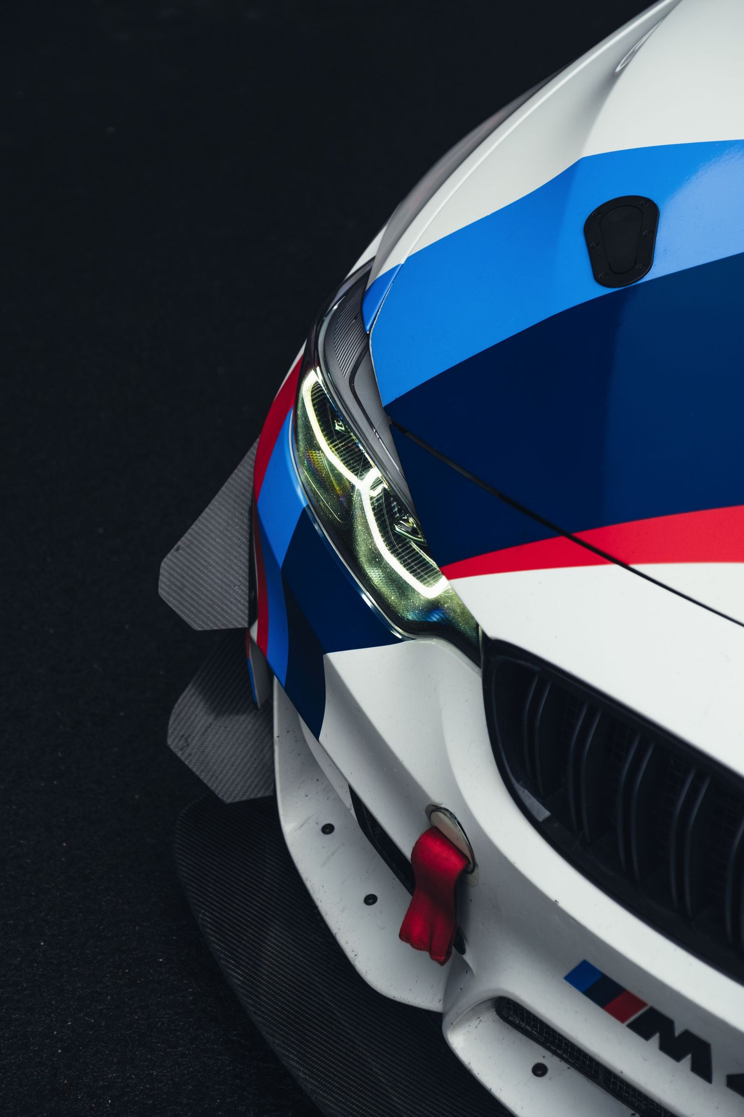 Close-up details of a white BMW M-series sports car with blue and red racing stripes.