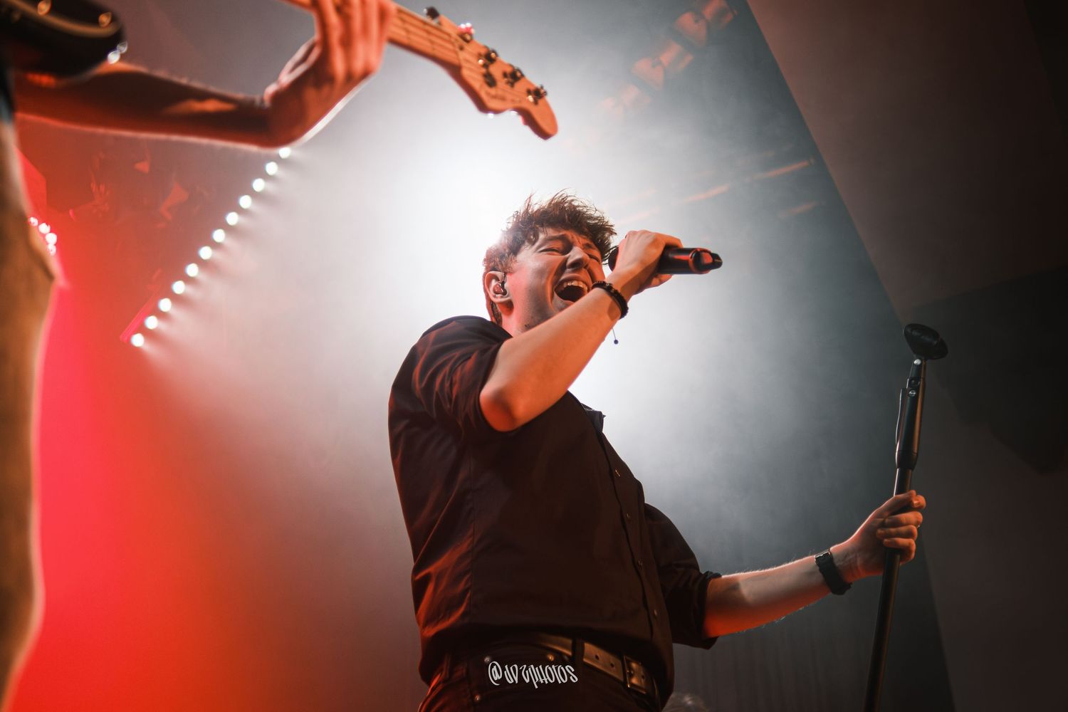 Dynamic concert photography capturing performer in dramatic red and white lighting.