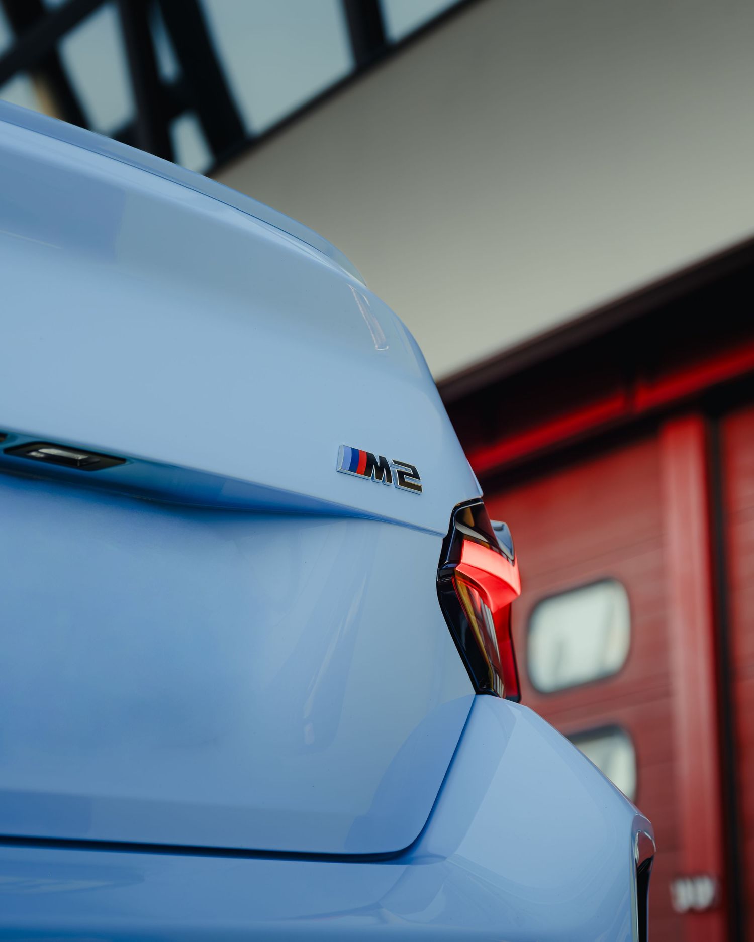 Close-up of BMW M2 badge on light blue sports car rear.