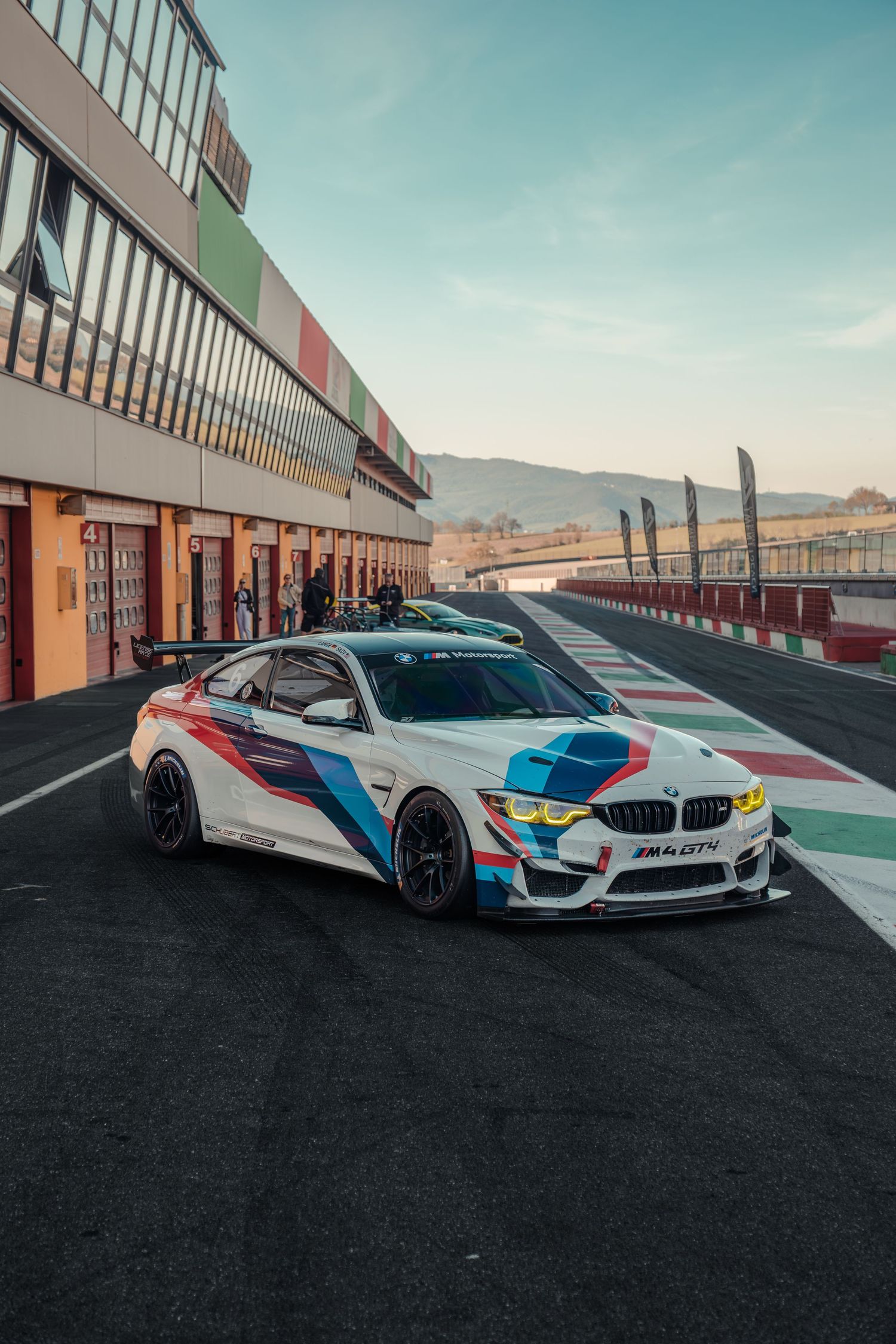 BMW M4 GT4 white racing car parked in pit lane at a professional motorsport circuit.