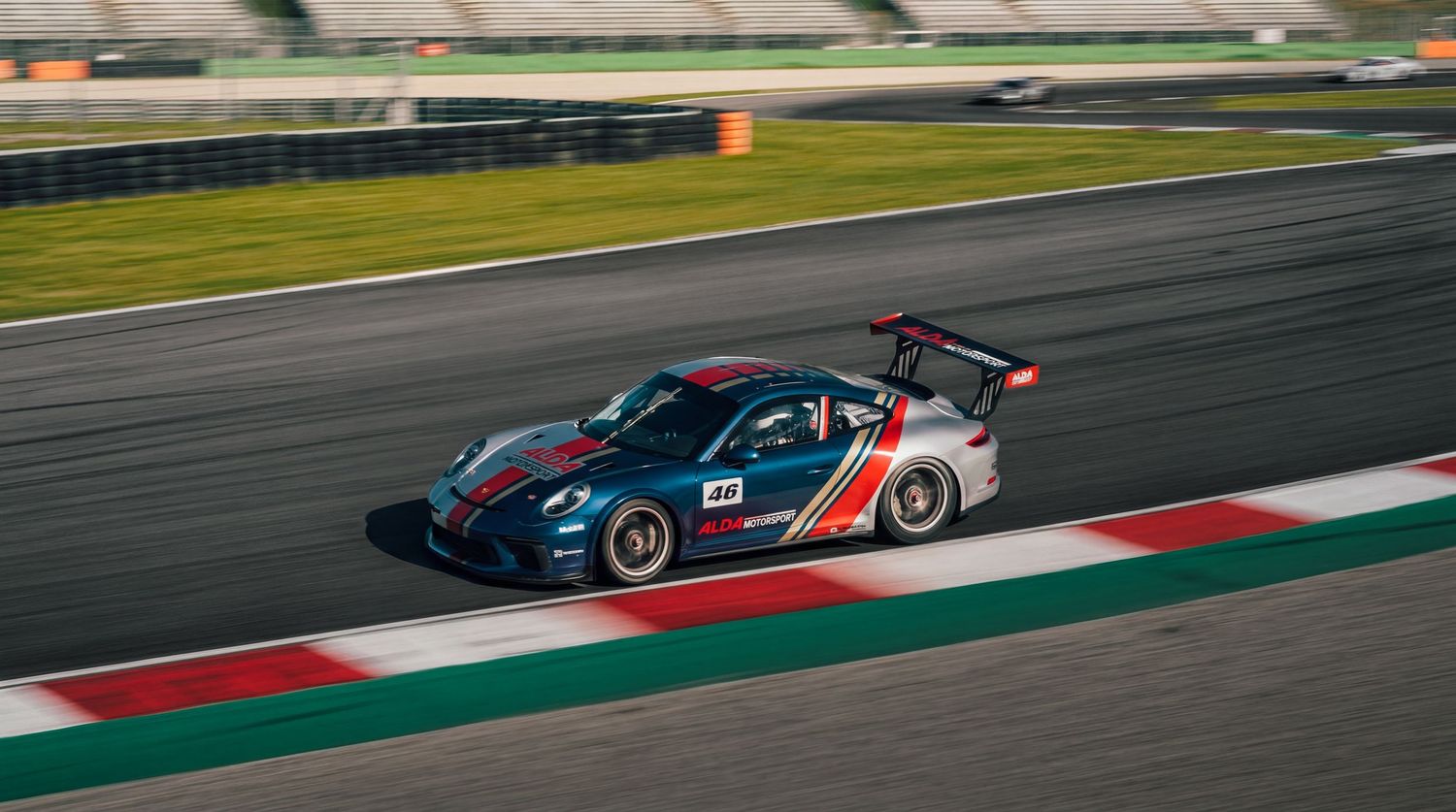 Dark blue Porsche race car with Martini livery speeding along a professional motorsport circuit.