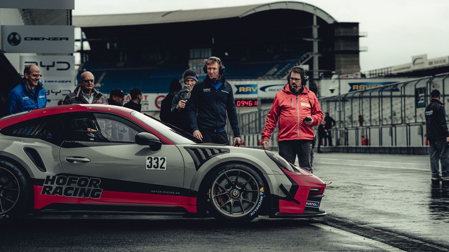 Panoramic view of race cars and pit crew at motorsport event.