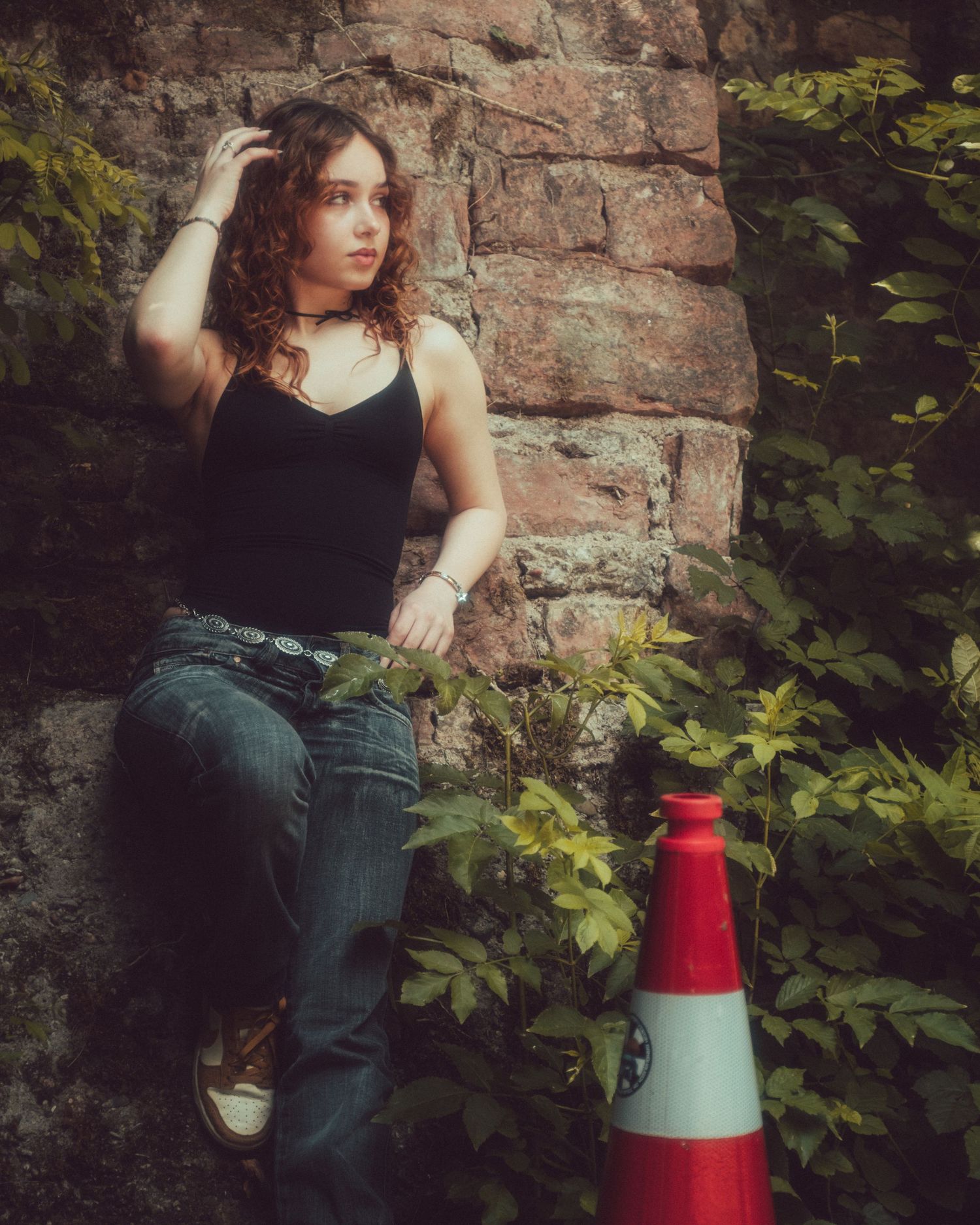 Outdoor portrait session against weathered brick wall with red traffic cone as prop.