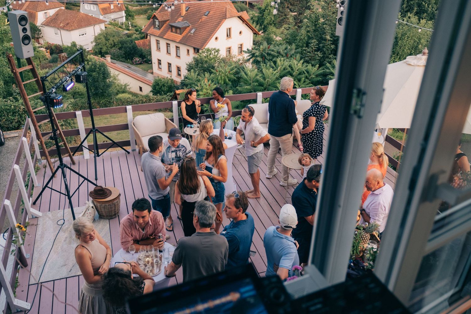 Elevated view of guests mingling on a terrace overlooking hills and buildings.