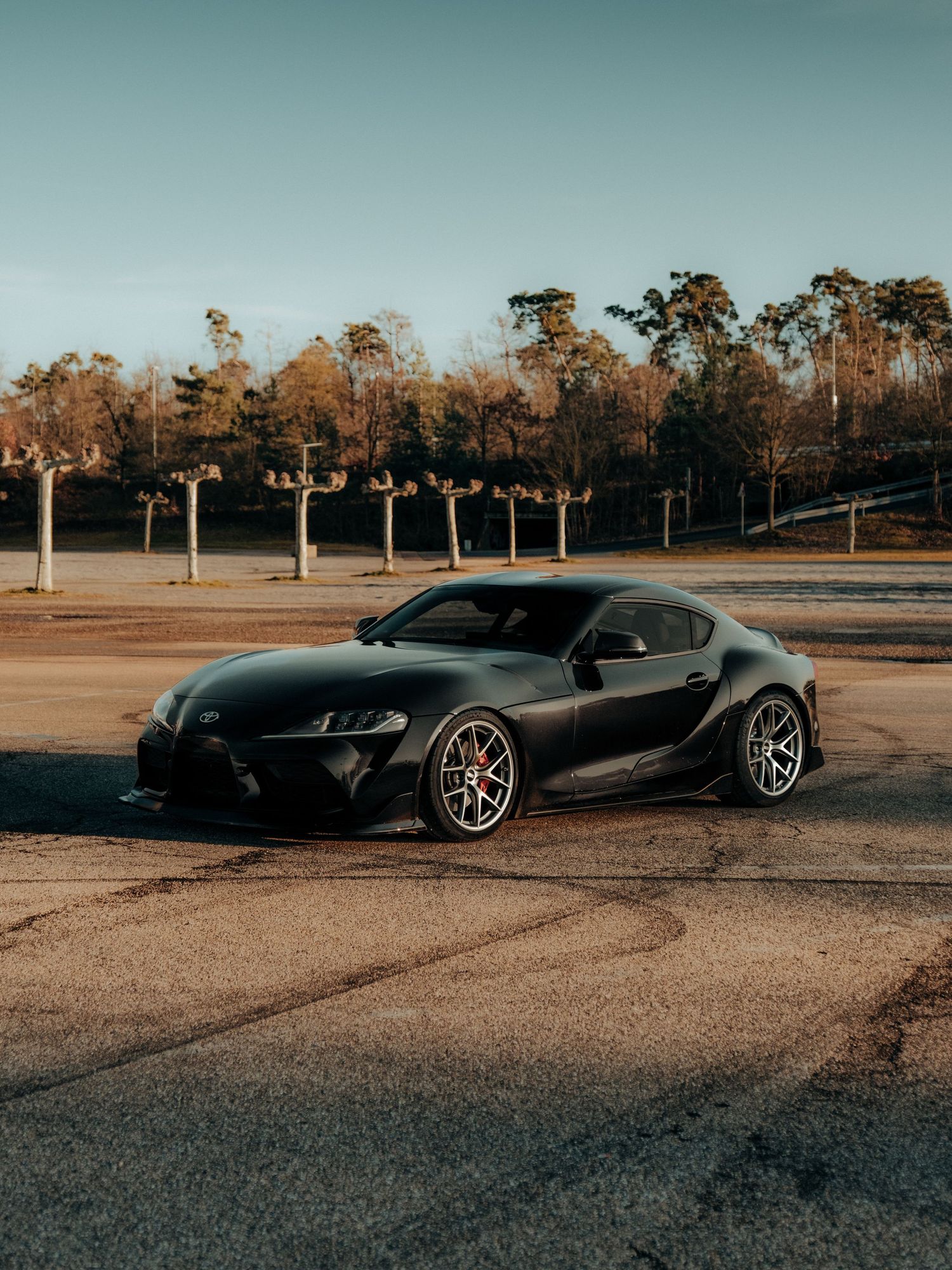 Black sports cars arranged in formation at sunset on an empty lot with trees in background.