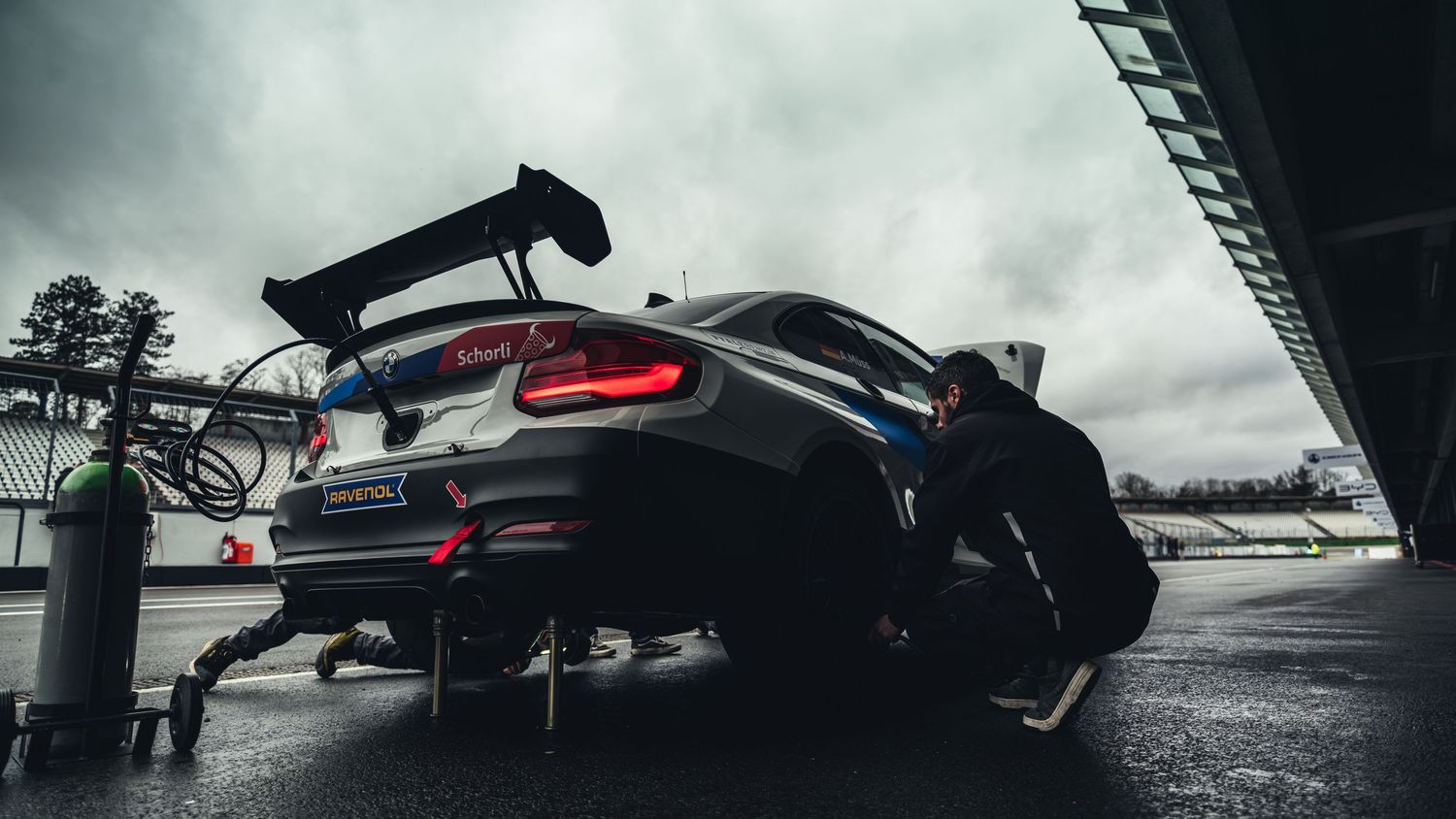 Panoramic view of race cars lined up under cloudy skies at a motorsport track.