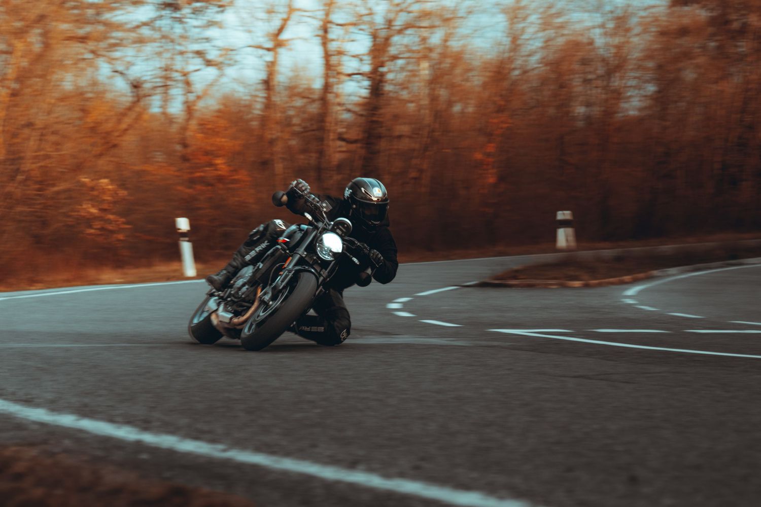 Motorcycle rider leans into a winding autumn road with orange foliage in the background during sunset.