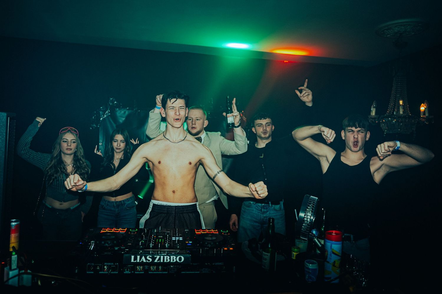 Concert crowd dancing in a dark venue with green and red stage lighting effects creating an energetic atmosphere.