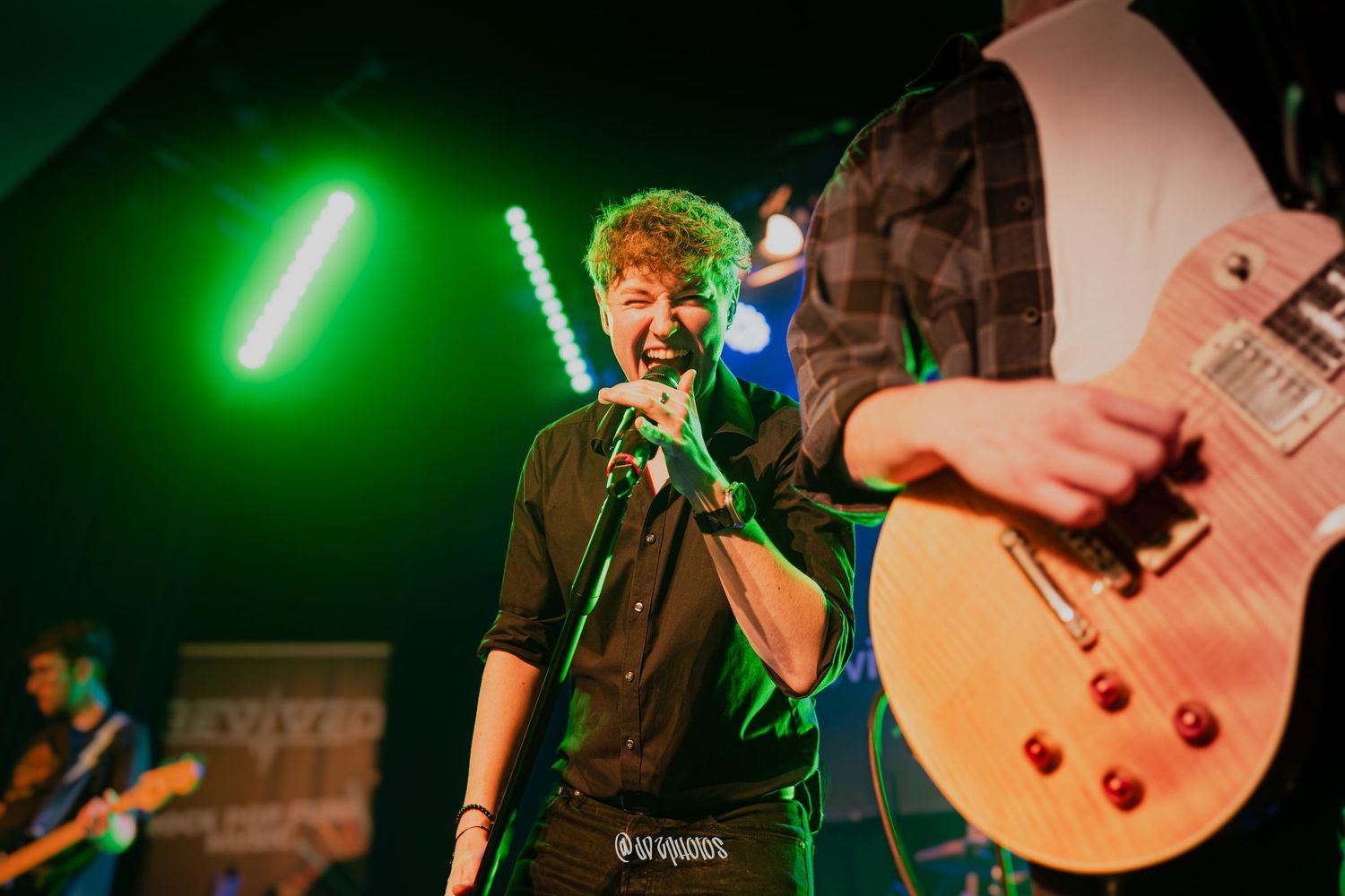Band members playing guitars on stage with green stage lighting creating an energetic atmosphere.