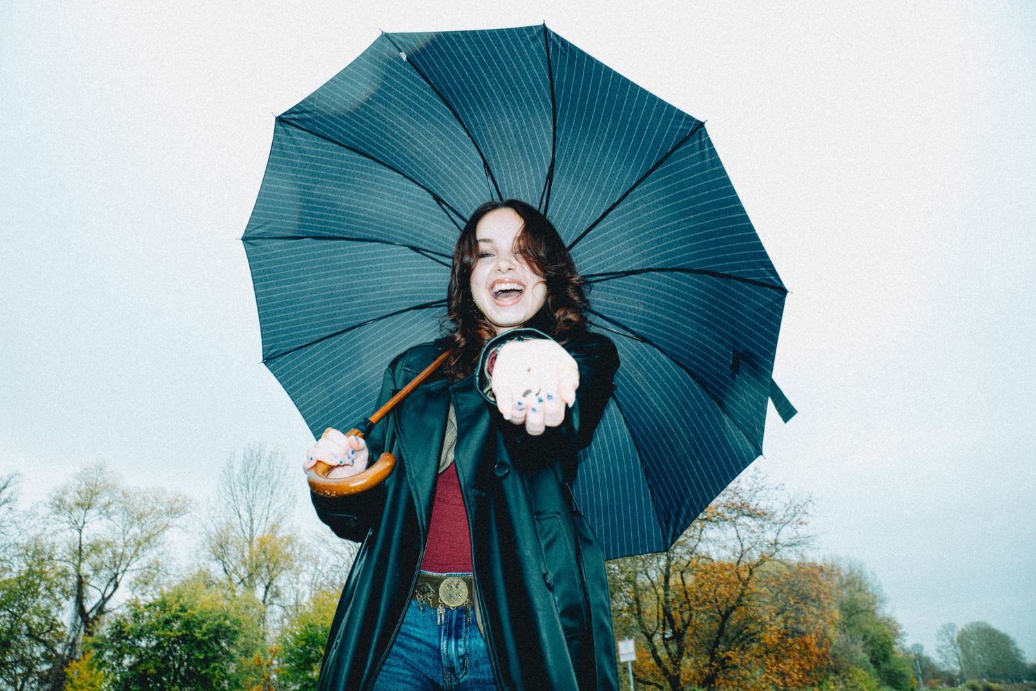 Teal umbrella against cloudy sky with autumn trees in background.