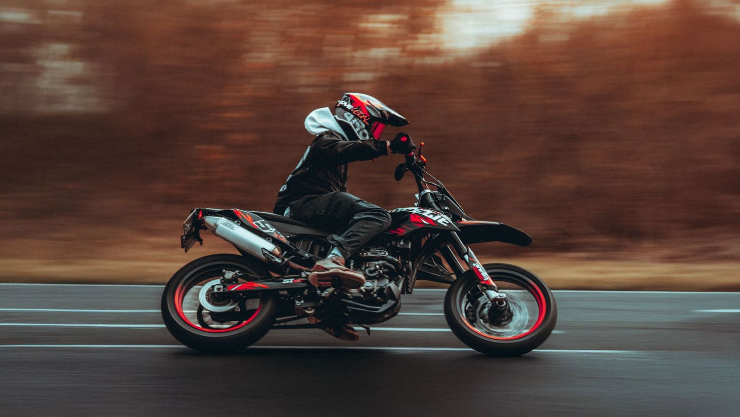 Black motorcycle racing through a curved road with autumn foliage in the background during golden hour.
