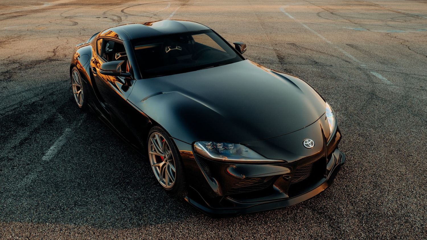 Low-angle panoramic view of black sports cars parked on asphalt at sunset.