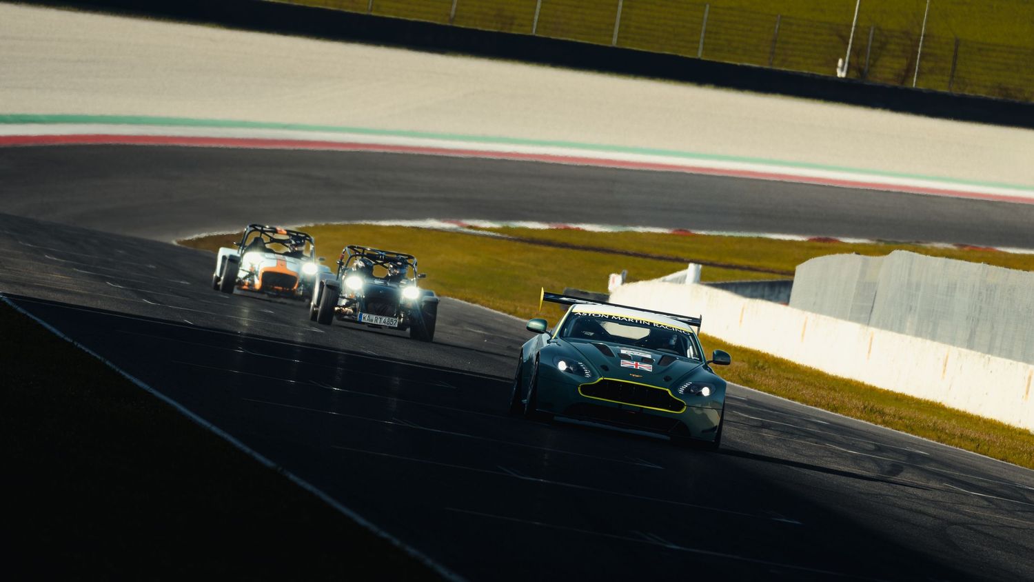 Aston Martin GT race car leading a pack of cars through a corner on a racing circuit.