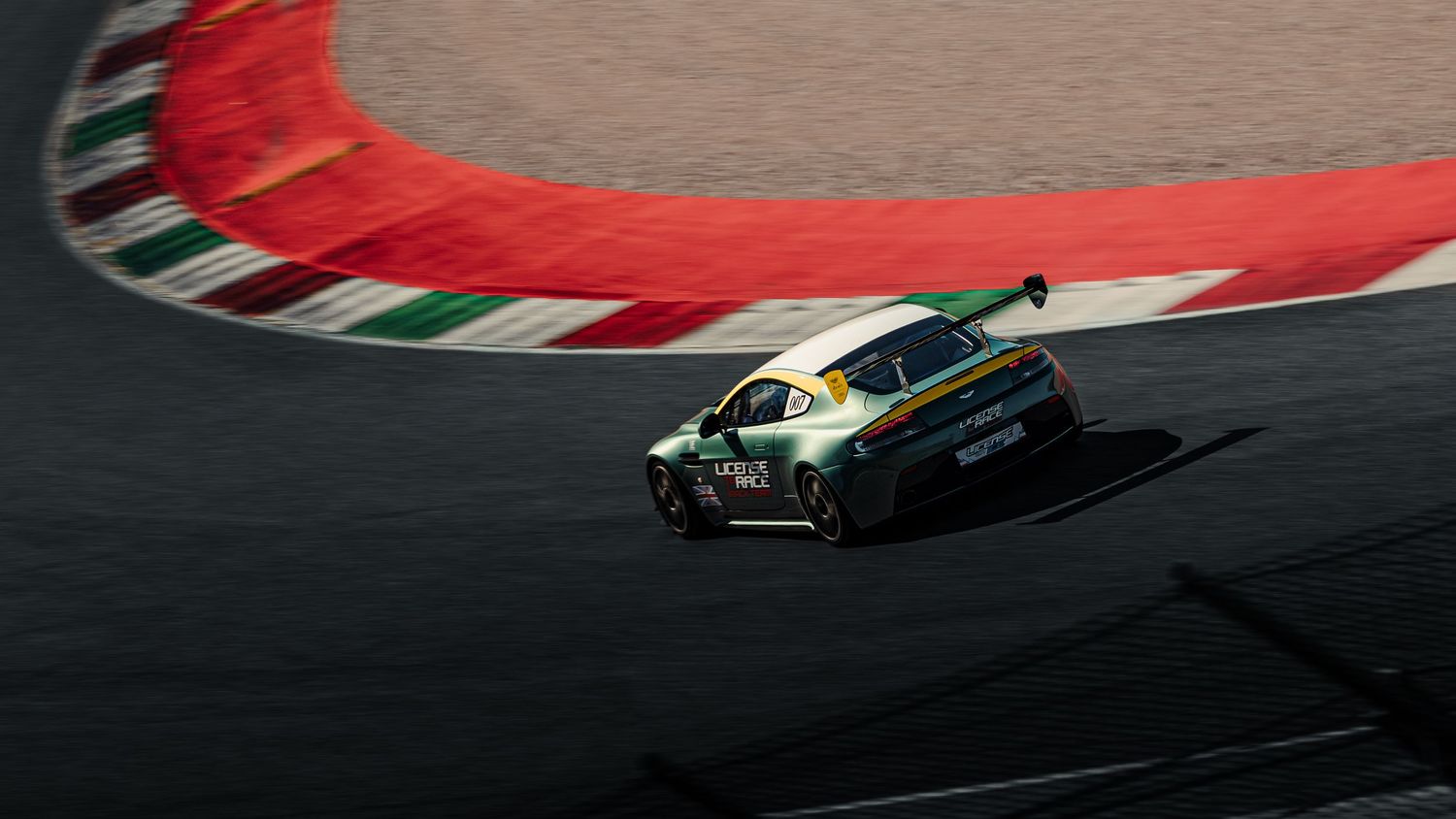 Green Aston Martin race car navigating a curve on a professional racing circuit track.