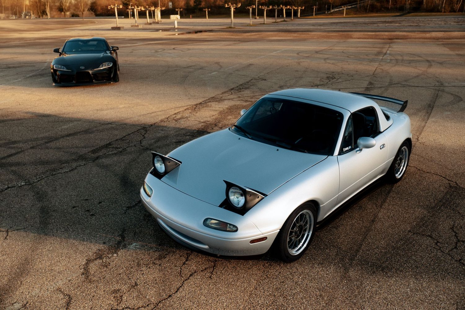 Collection of classic and modern sports cars displayed in warm evening light on dirt surface.