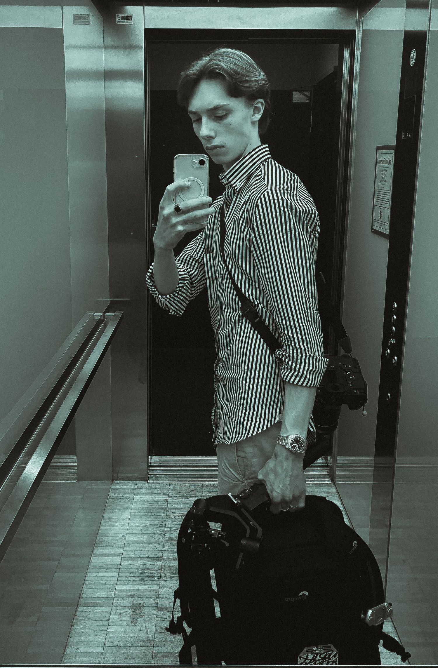 Security camera view of person in striped shirt using phone near elevator.