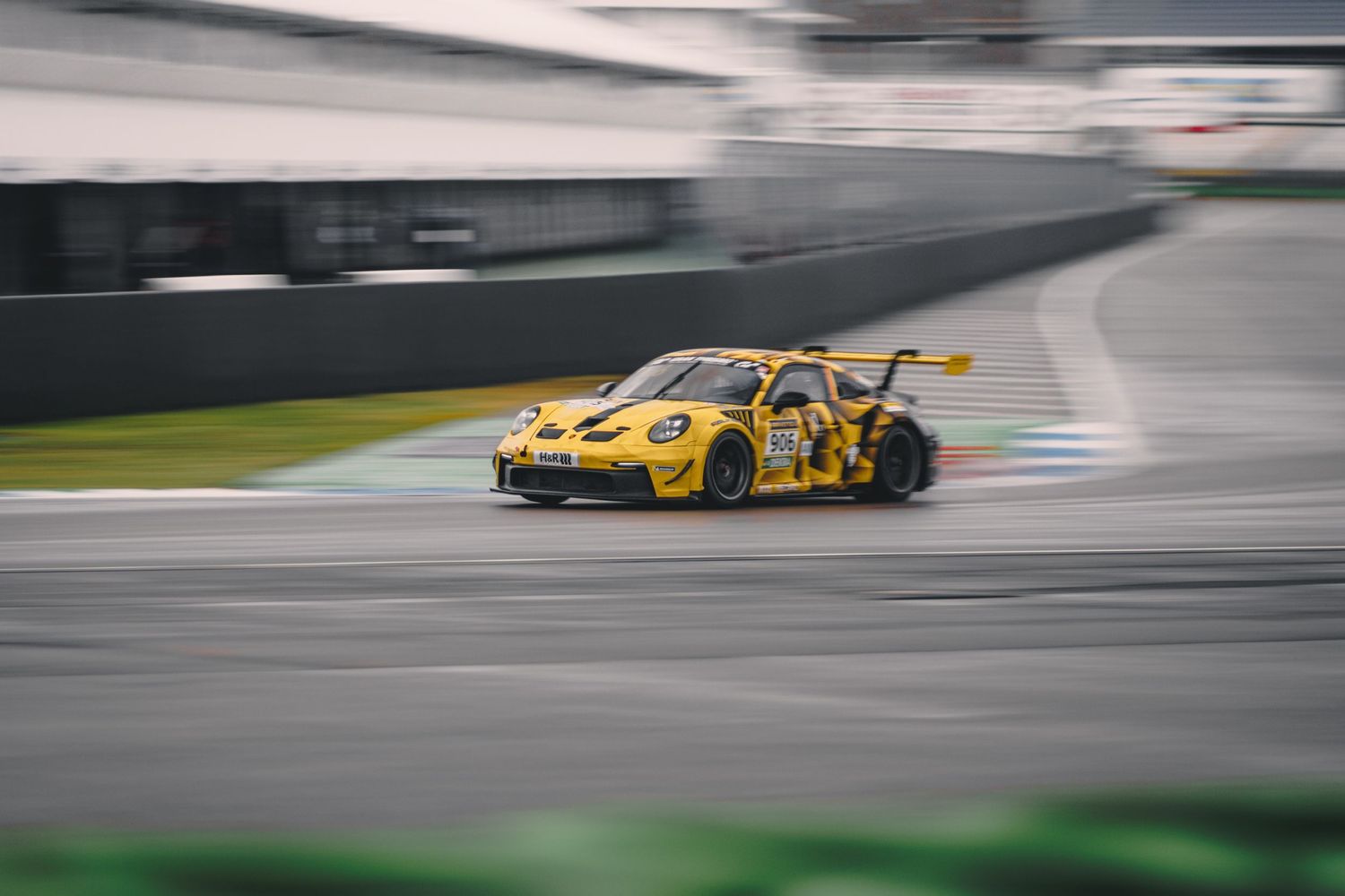 Yellow Porsche race car in motion on a wet race track during competition.