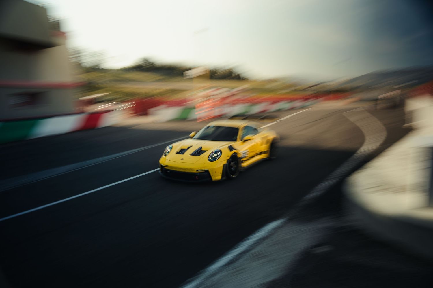 Yellow Porsche 911 GT3 racing through a corner on a professional race track.