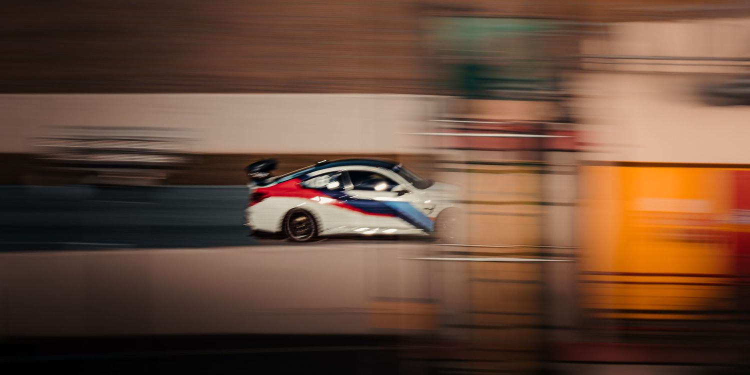A white BMW race car speeds around a track at night, captured with motion blur effect.