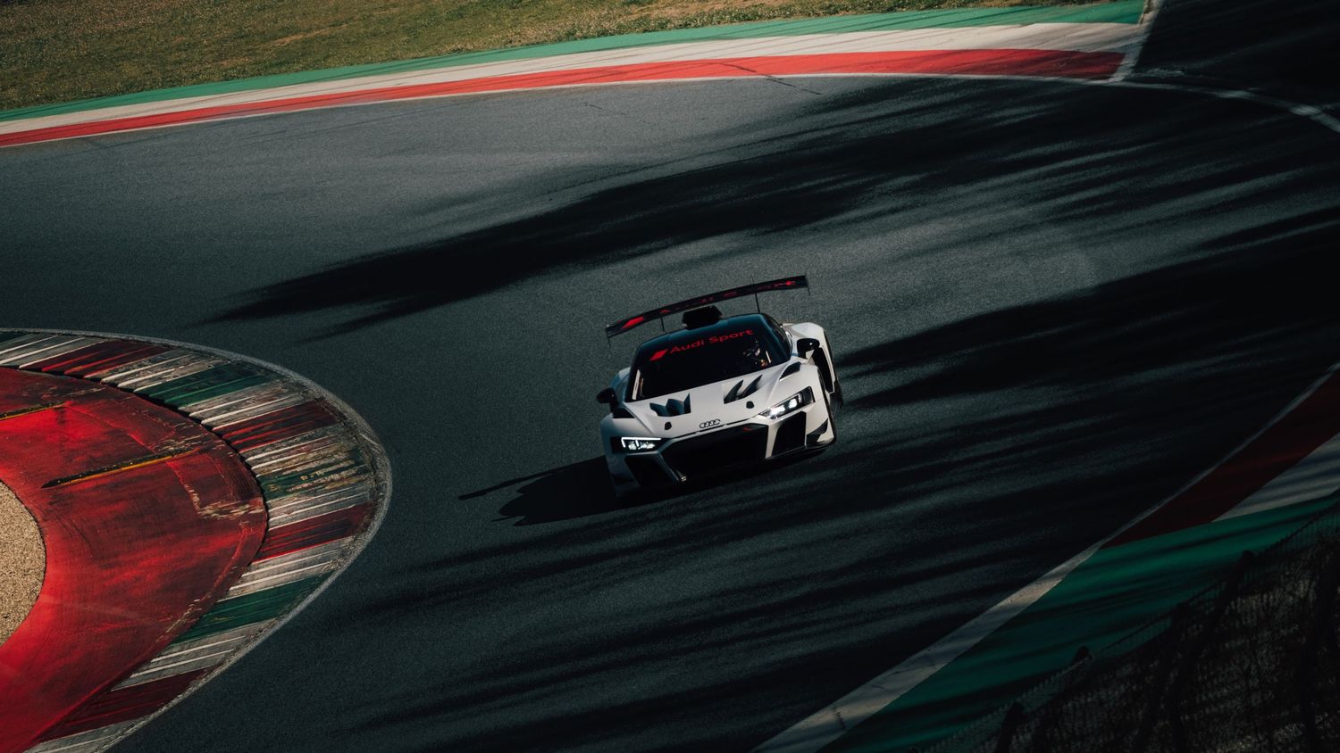 White race car speeding on a professional racing circuit track from aerial view.