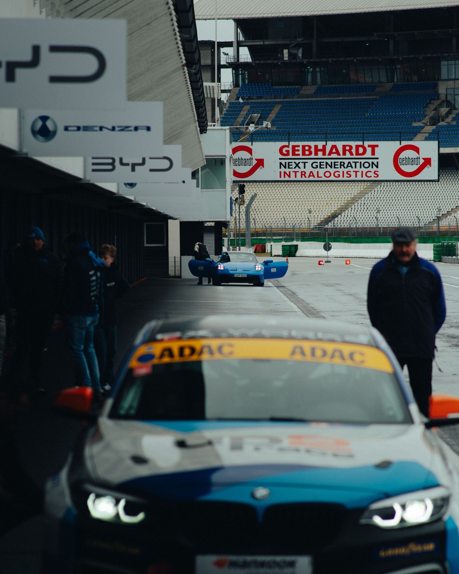 Racing scene at track with BMW vehicles and sponsorship banners visible.