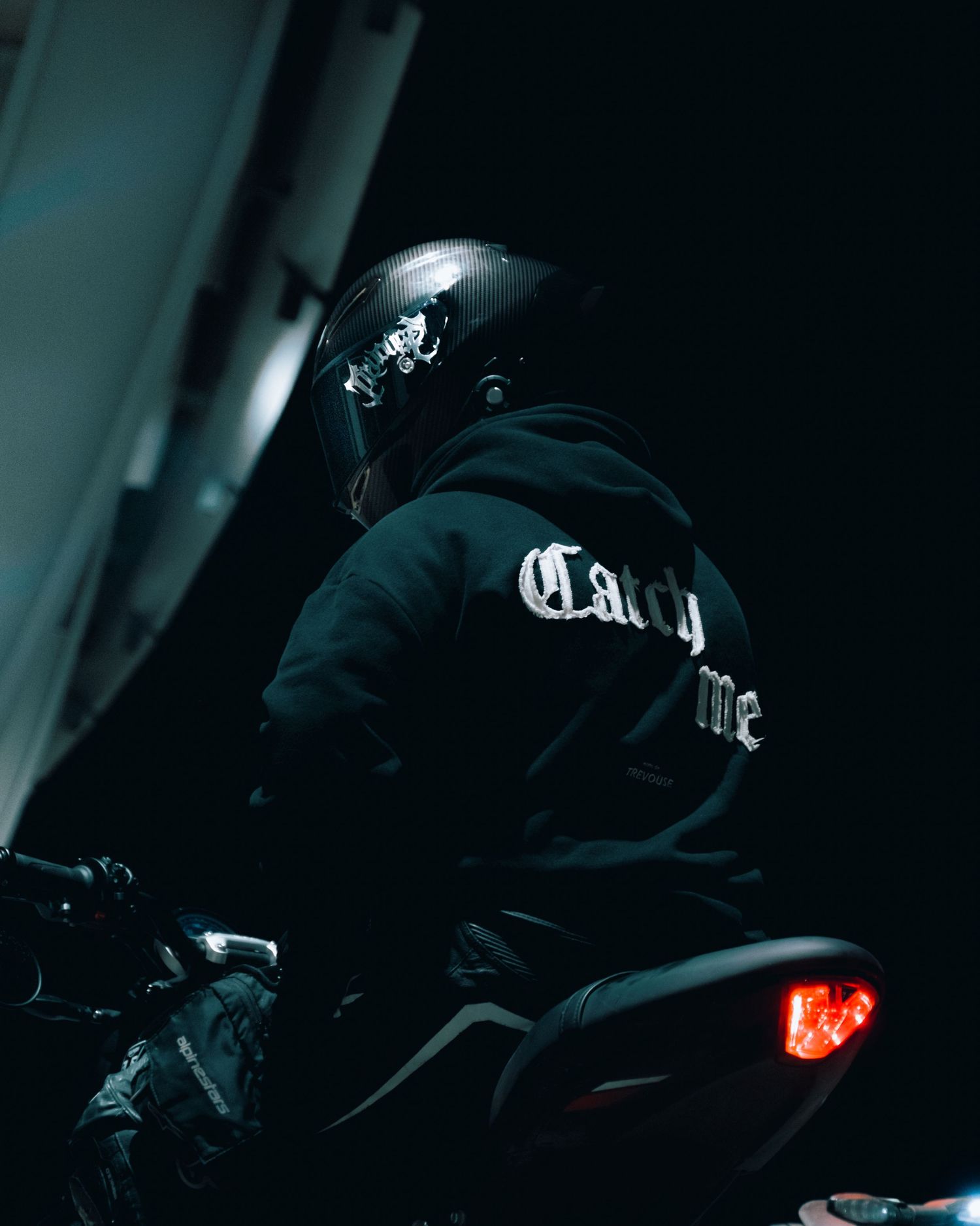 Dark silhouette of a motorcycle rider with glowing tail light at night.