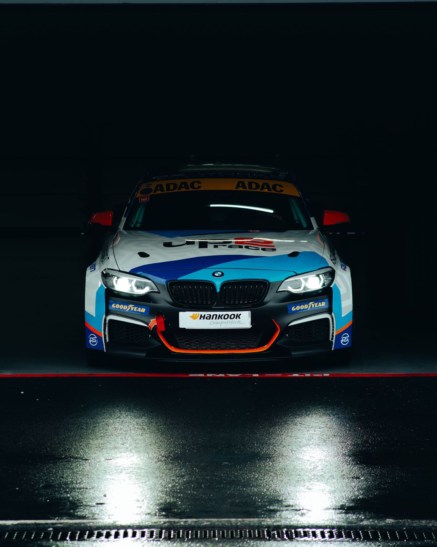 BMW M racing car with custom livery and sponsorship decals photographed in dark studio lighting.