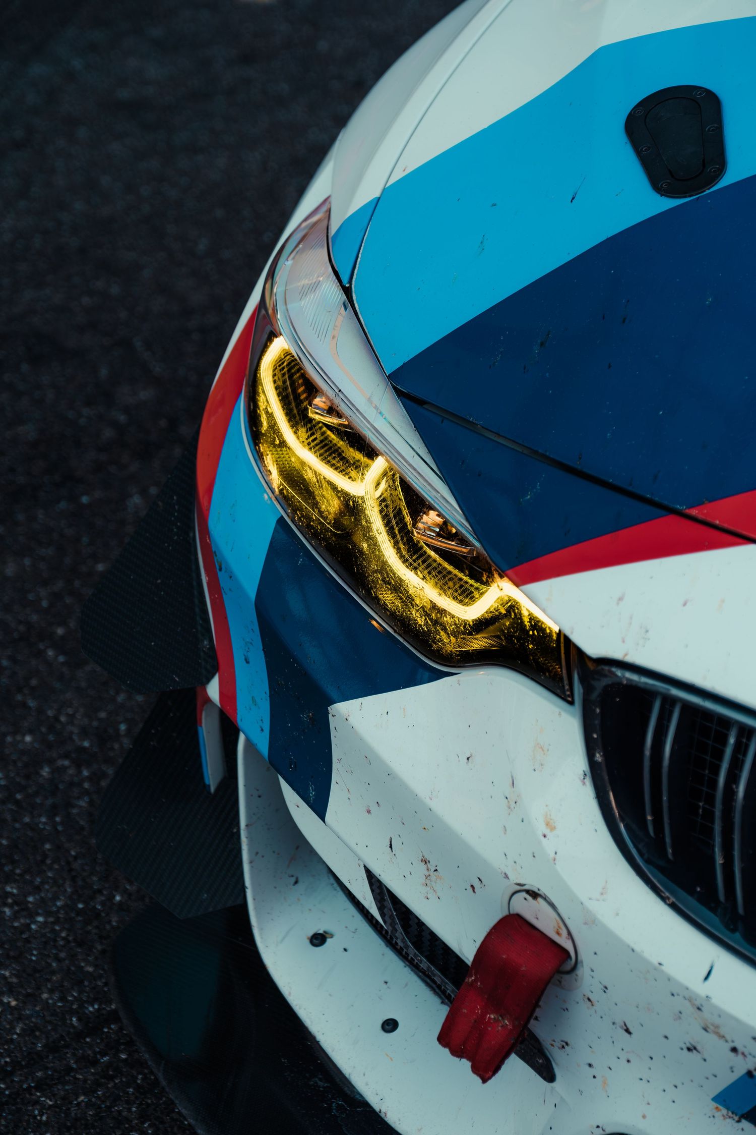 Close-up of a BMW M Motorsport race car headlight with yellow LED detailing and race livery.