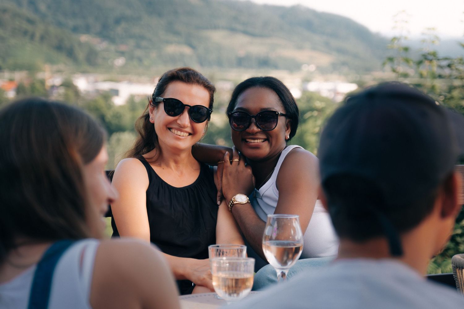 Friends socializing at outdoor restaurant with mountain views.