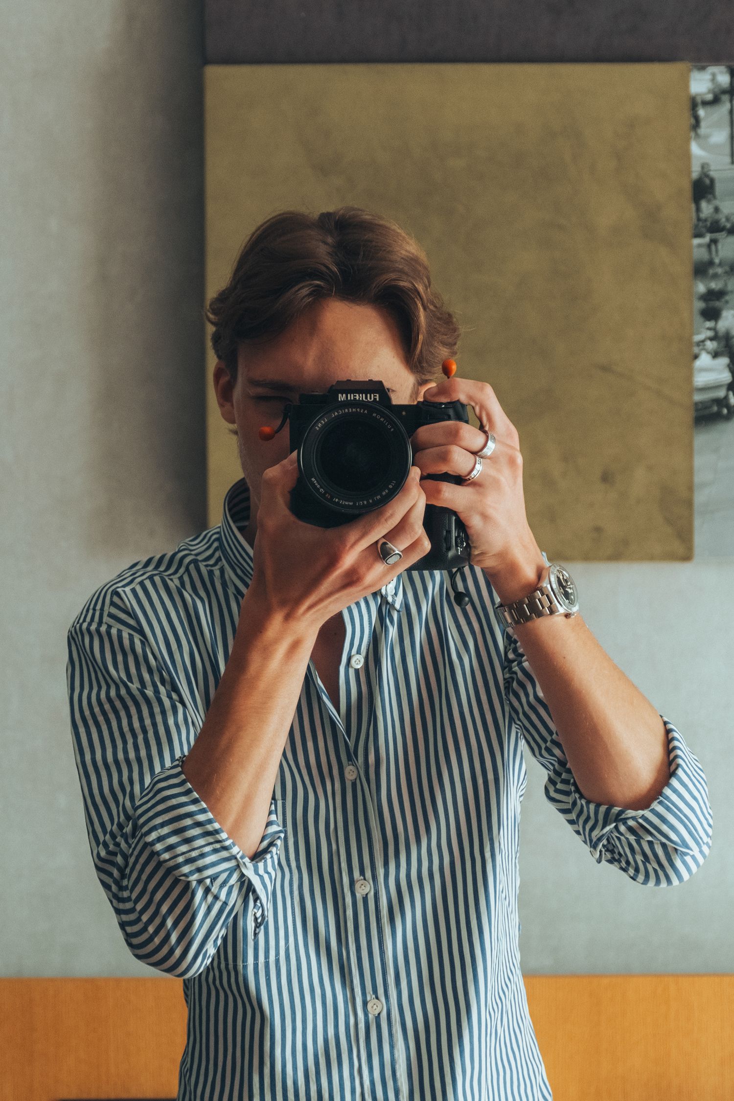 Person taking a photo with a professional camera wearing a striped button-down shirt.