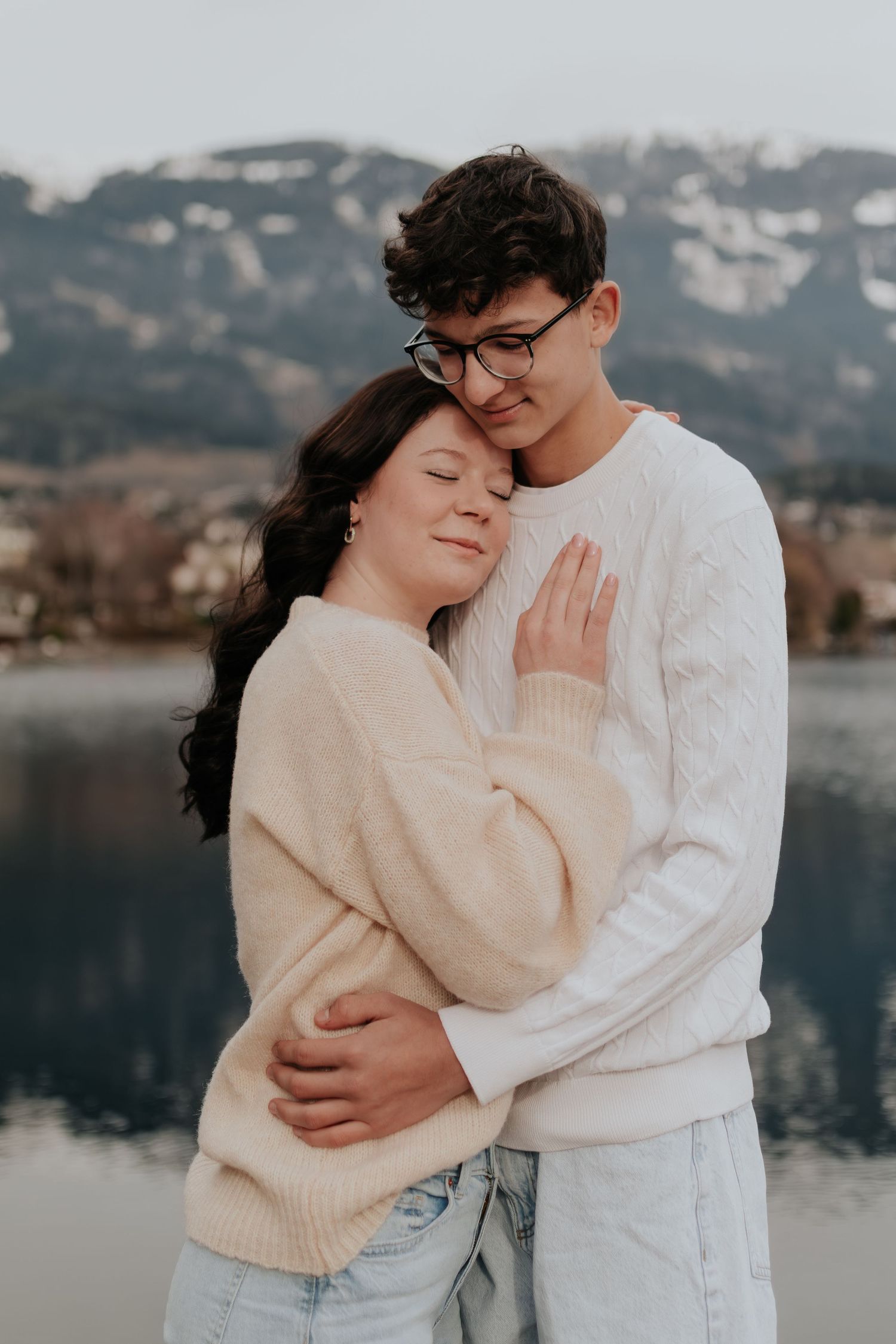 Eine intime Umarmung zwischen einem Paar, das gemütliche Pullover an einem Bergsee trägt.