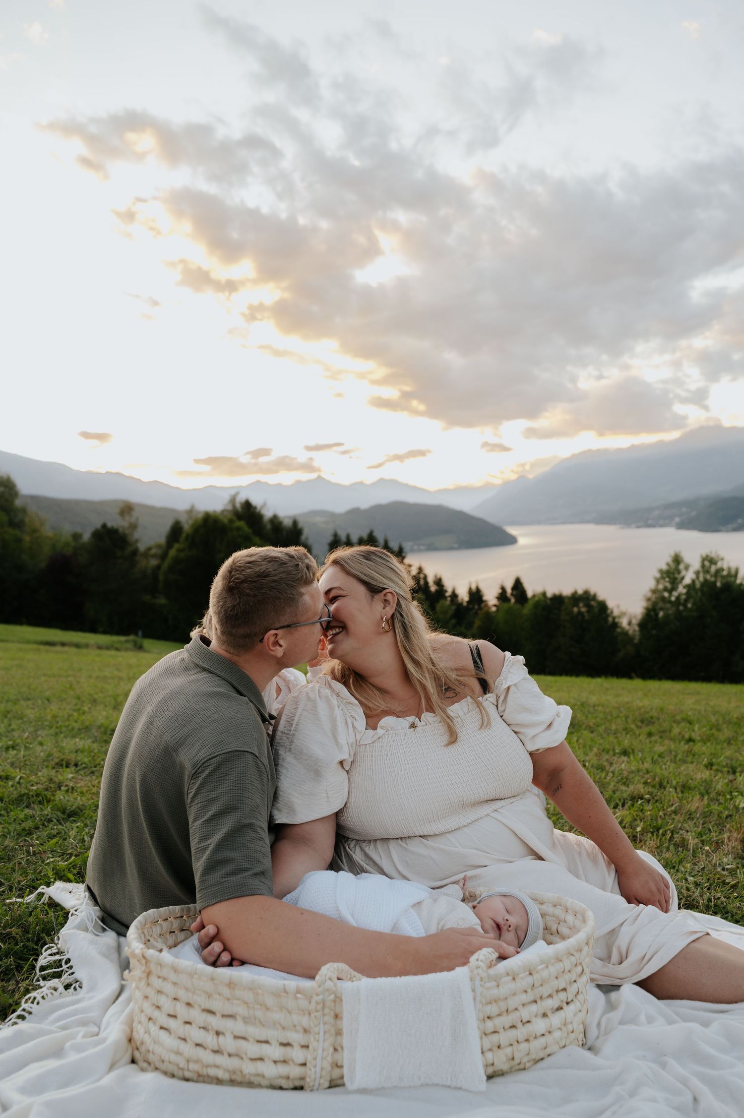 Couple sharing a romantic moment on a blanket at sunset with mountain lake views in background.