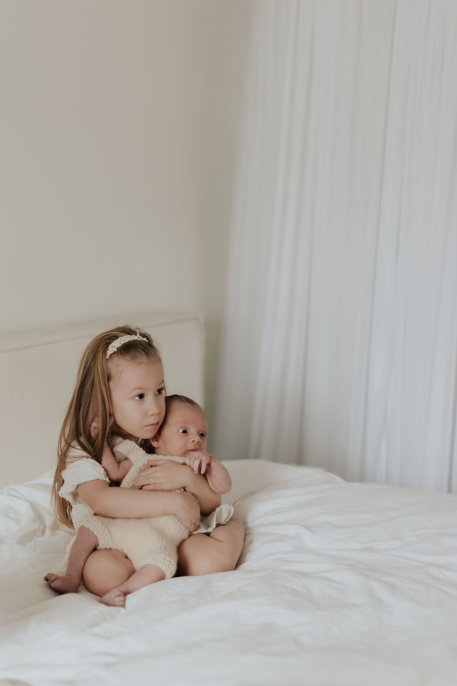 Two young siblings share sweet moments together while playing on a white bed.