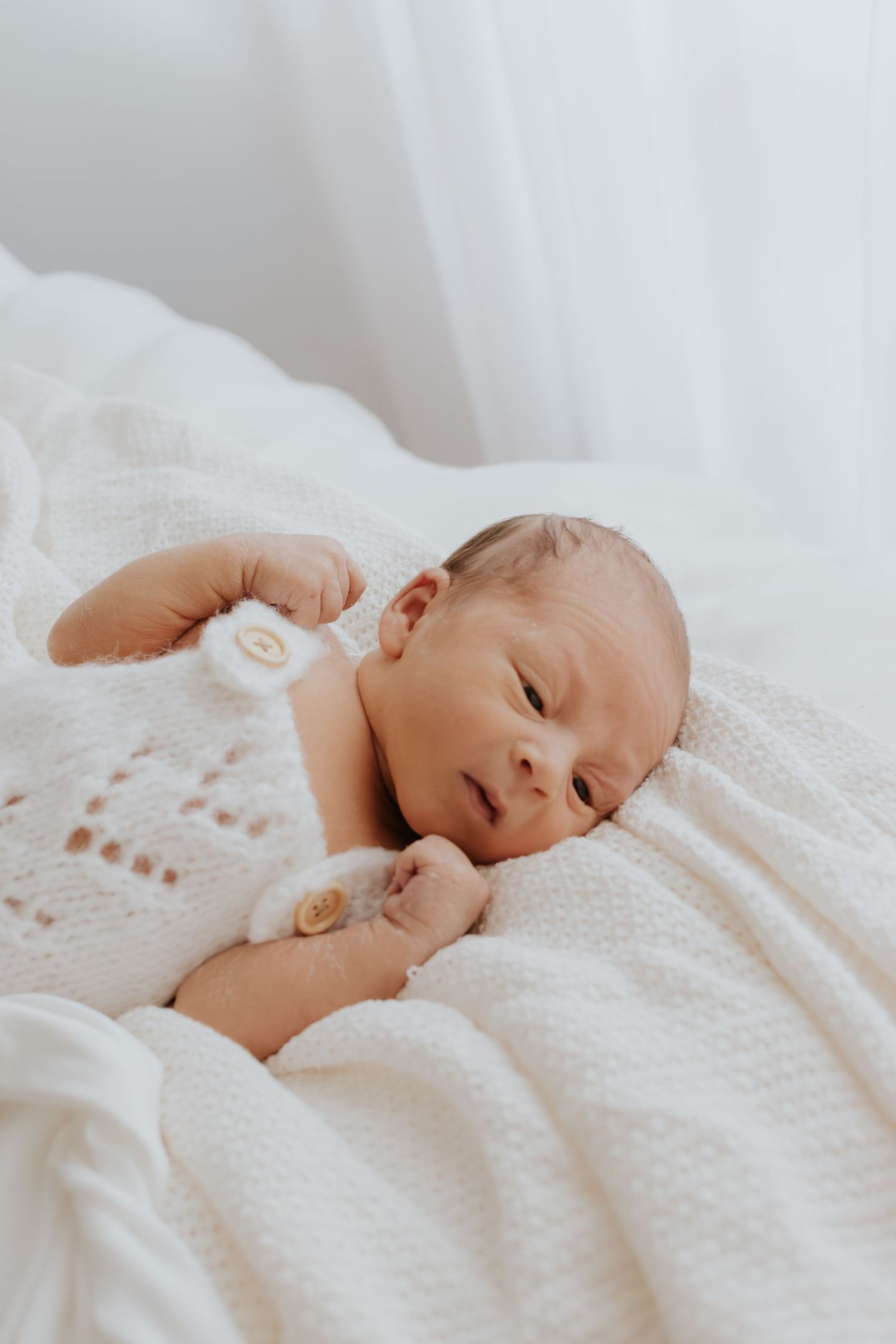 Peaceful newborn baby sleeping on soft white textured blanket in natural light.
