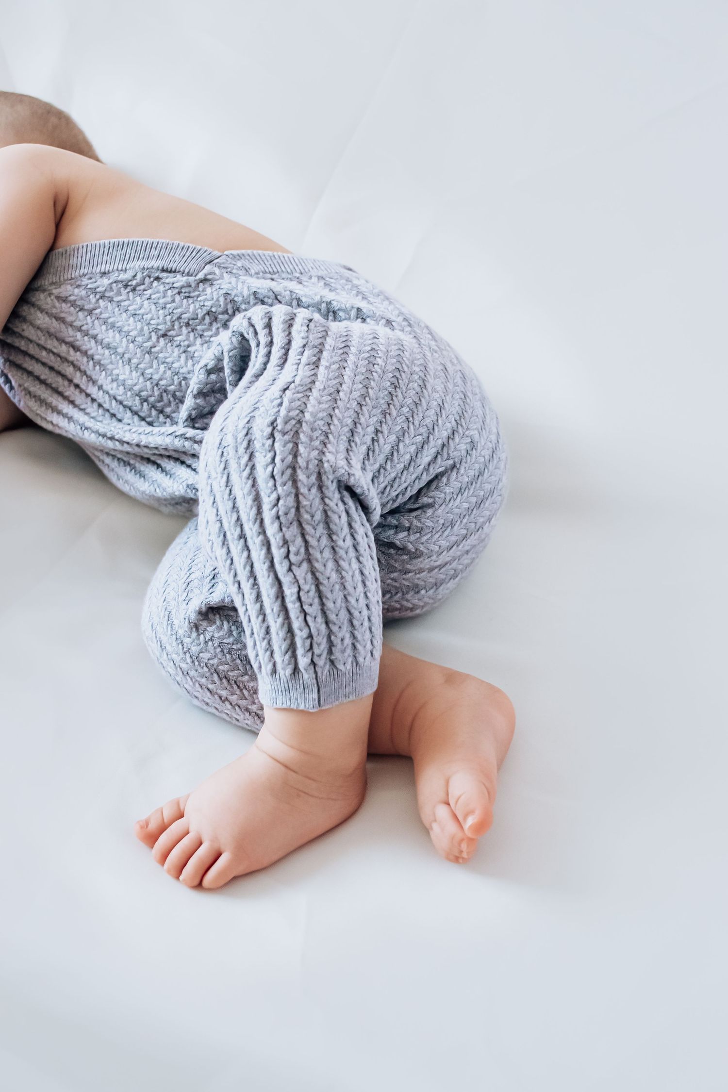 Adorable baby legs wearing cozy gray knit leg warmers against a white background.