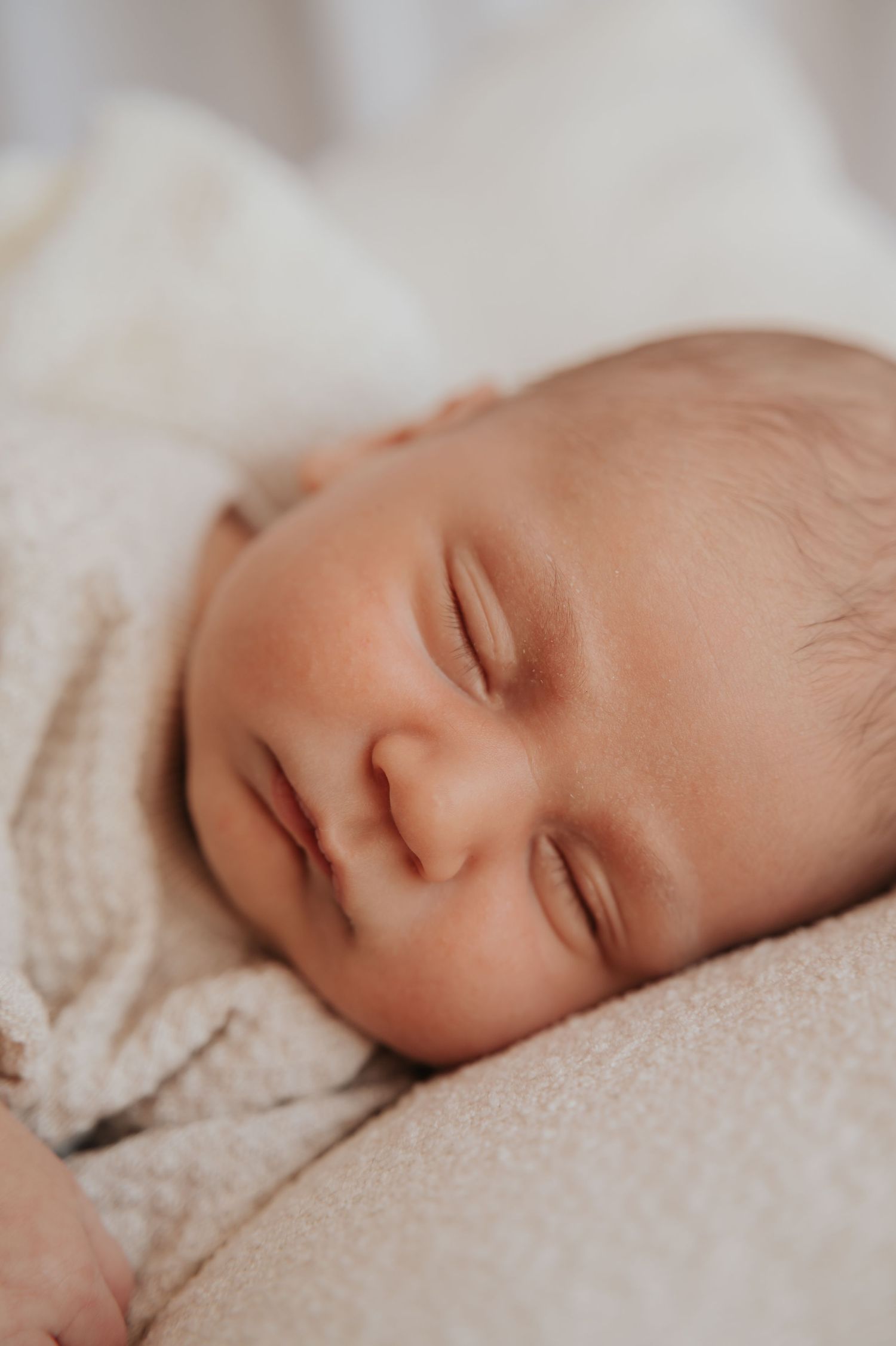 Close-up of a sleeping newborn baby with soft skin resting on a cream blanket.