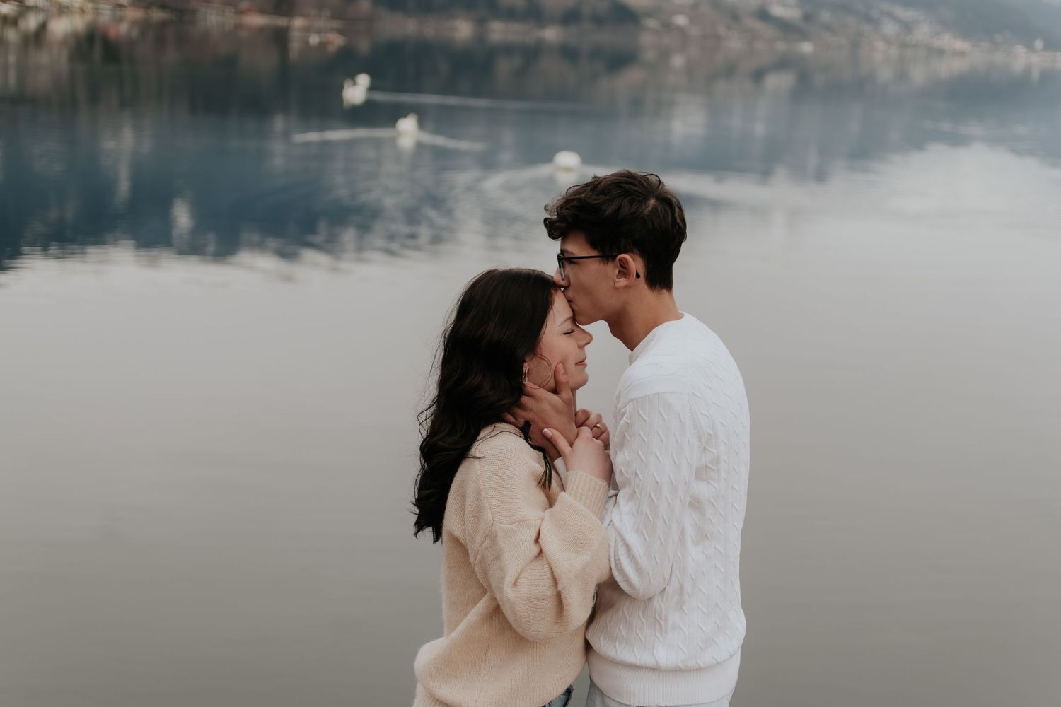 Romantic couple embracing near a serene lake, sharing a tender moment outdoors in soft natural light.