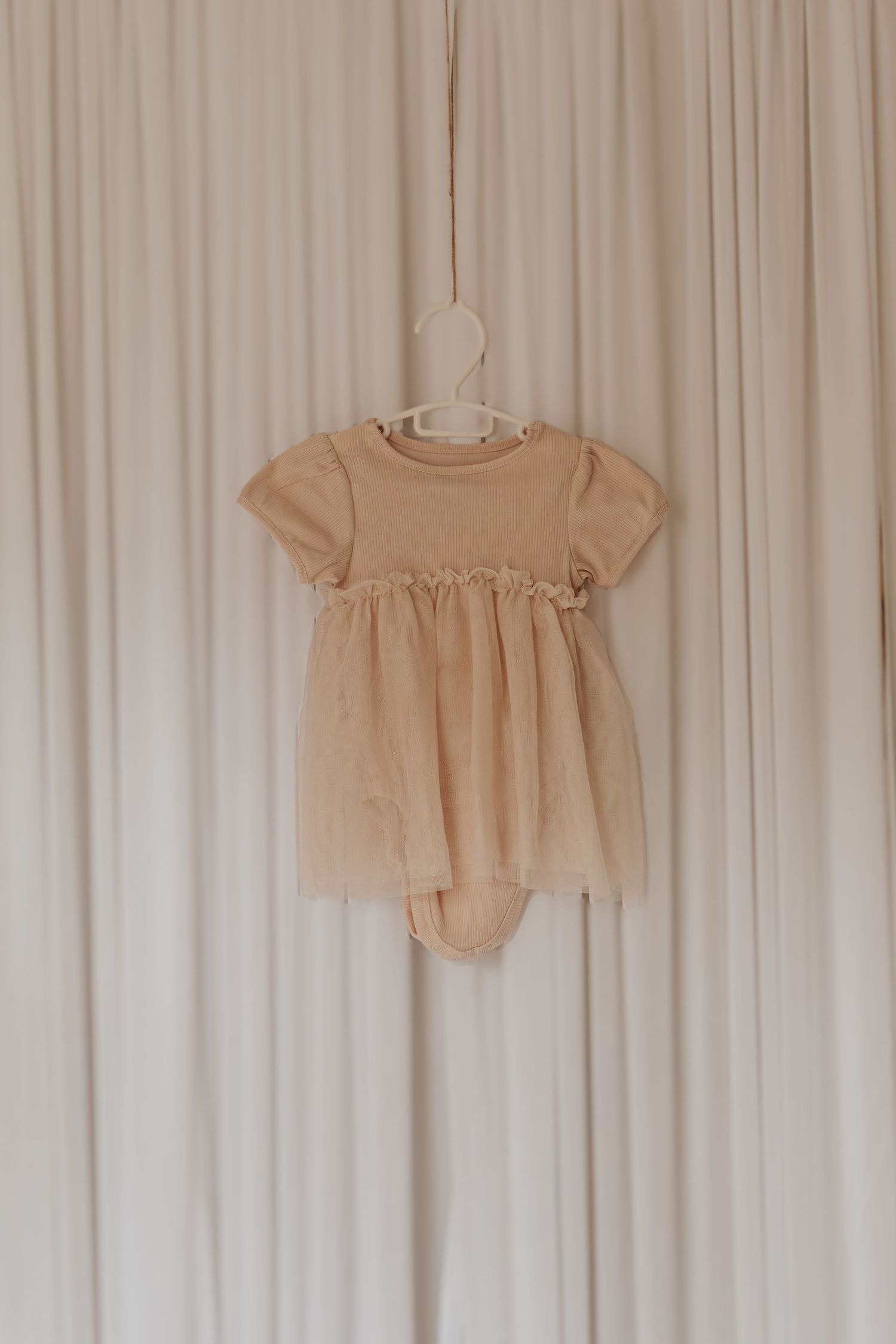Beige und nackte Blus, die an einem weißen Vorhanghintergrund hängen, zeigen minimalistisches Mode-Styling.