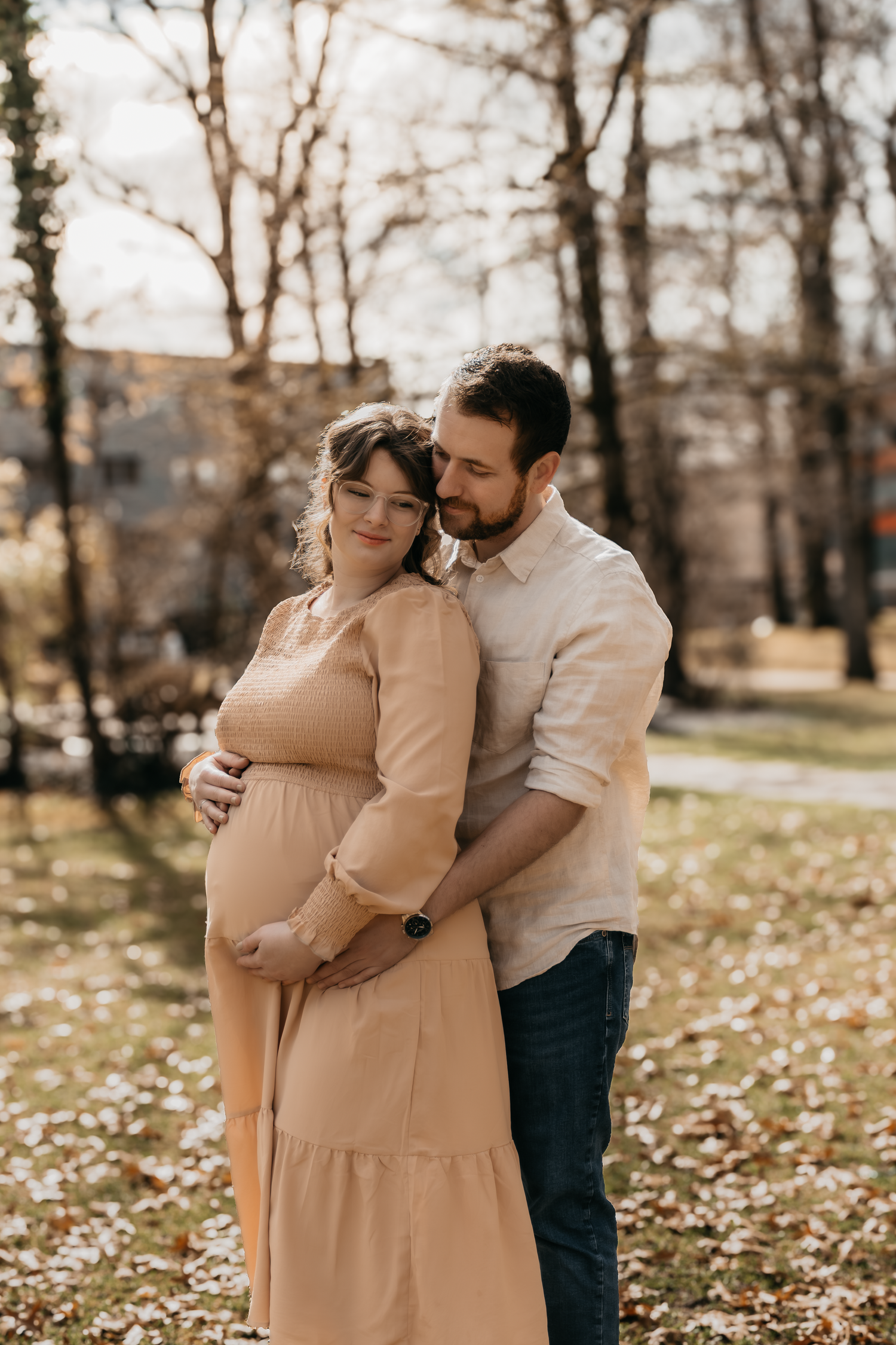 Intimes Mutterschafts-Fotoshooting im Freien mit einem Paar, das sich an gefallenen Herbstblättern umarmt.