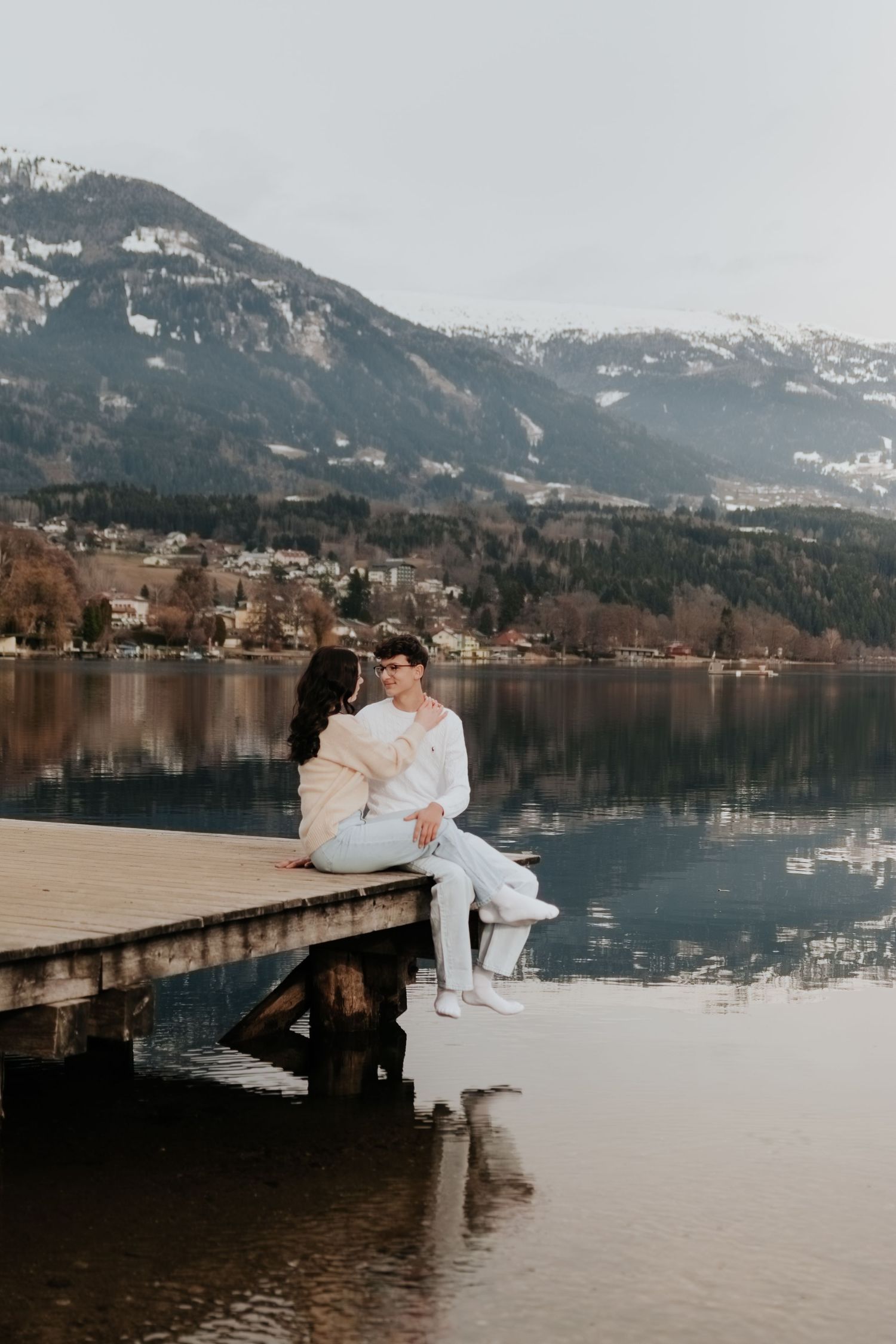 Ein Paar sitzt zusammen auf einem Holzdock mit Blick auf einen ruhigen Bergsee.