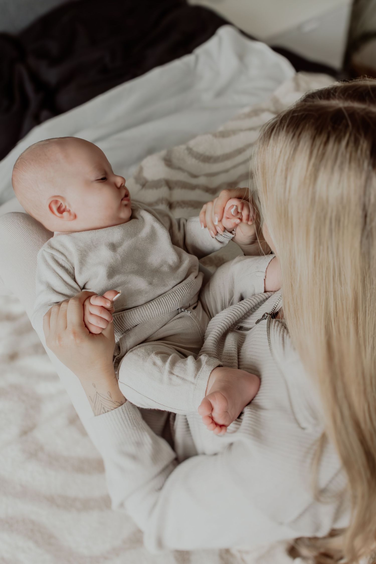 A tender moment between parent and sleeping newborn baby in soft white bedding.