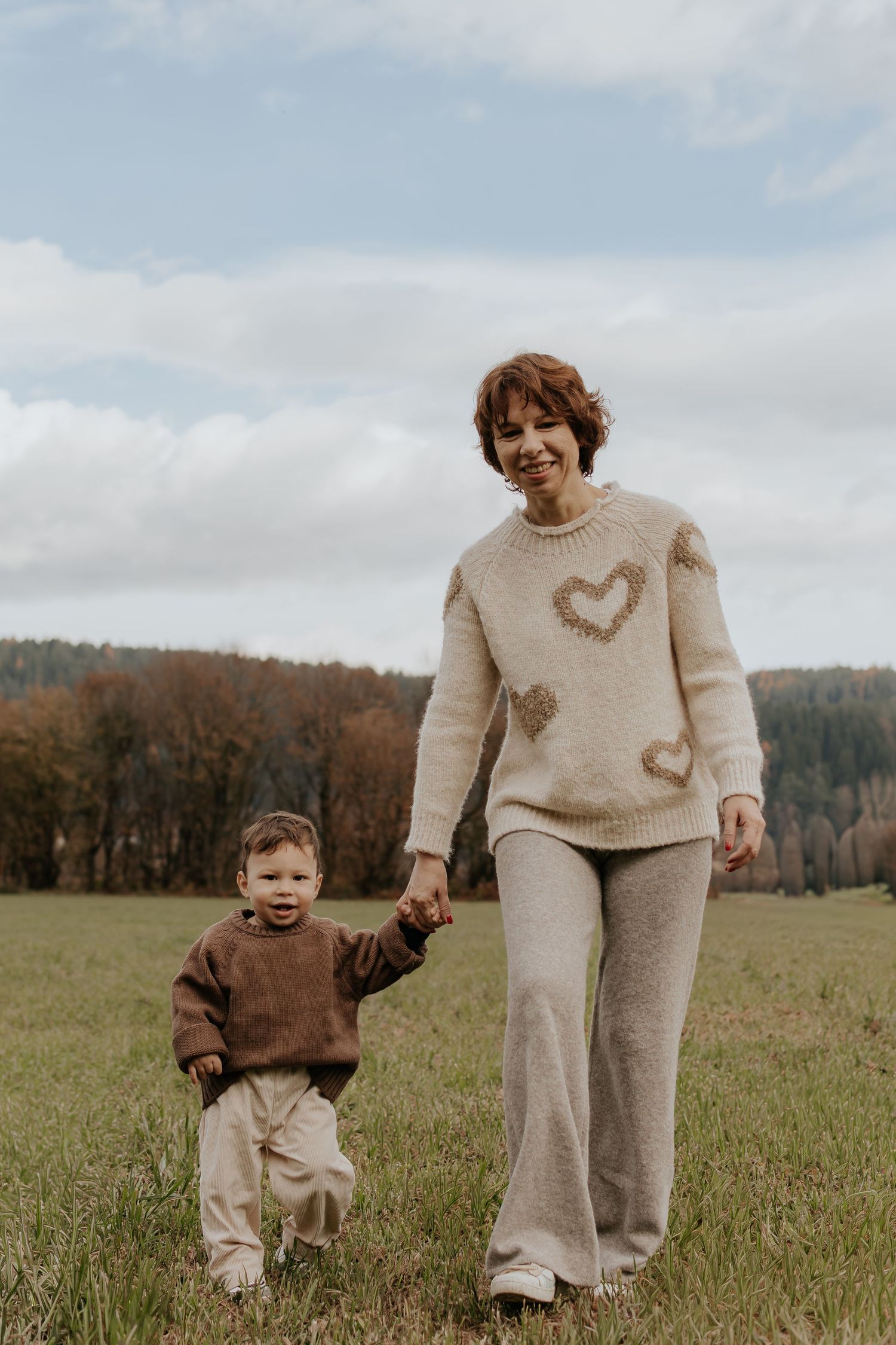 Ein herzerwärmender Familienmoment, der auf einer Wiese festgehalten wurde, in aufeinander abgestimmten cremefarbenen und braunen Pullovern.