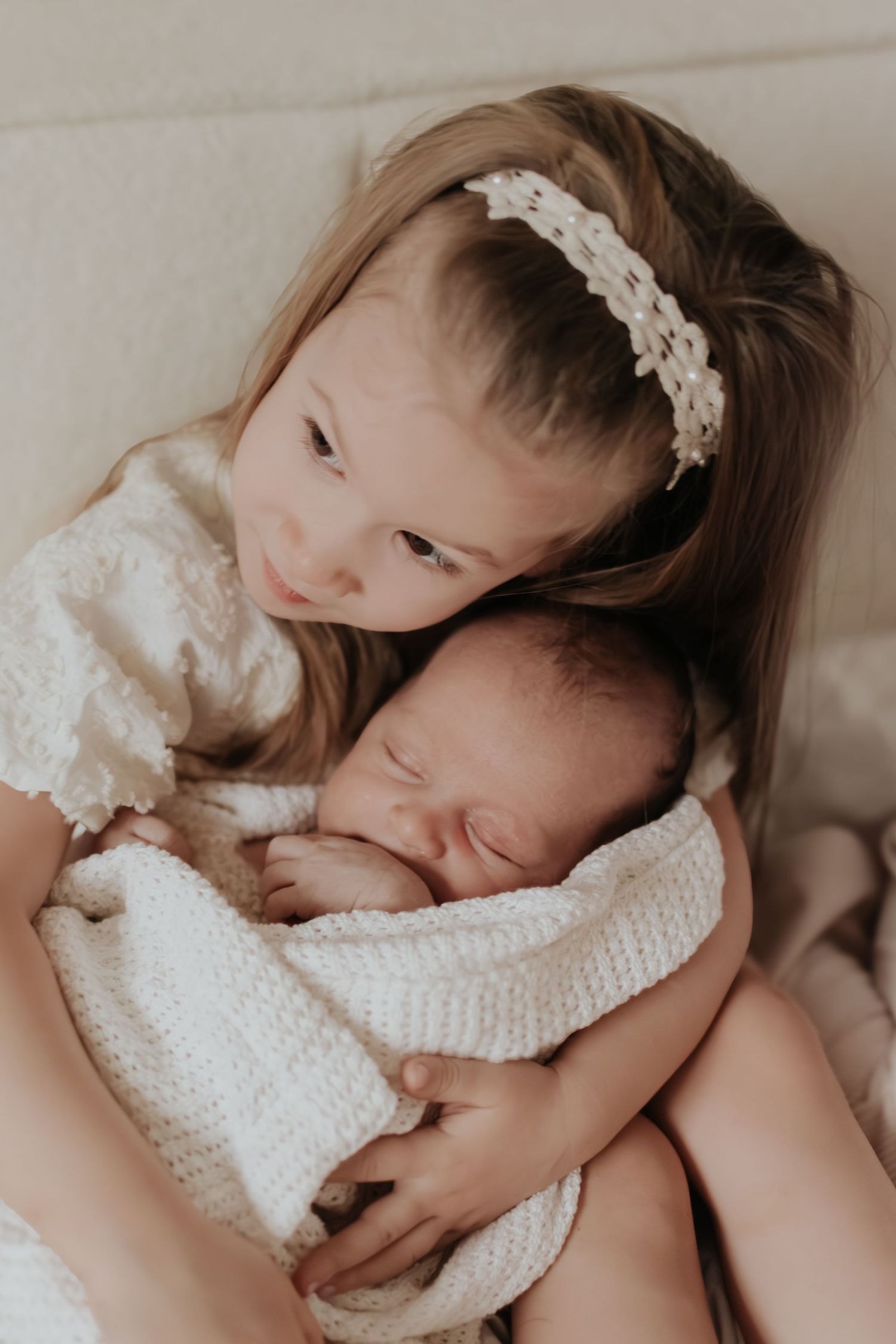 A newborn baby wearing a white knit outfit and lace headband rests peacefully in a series of gentle poses.