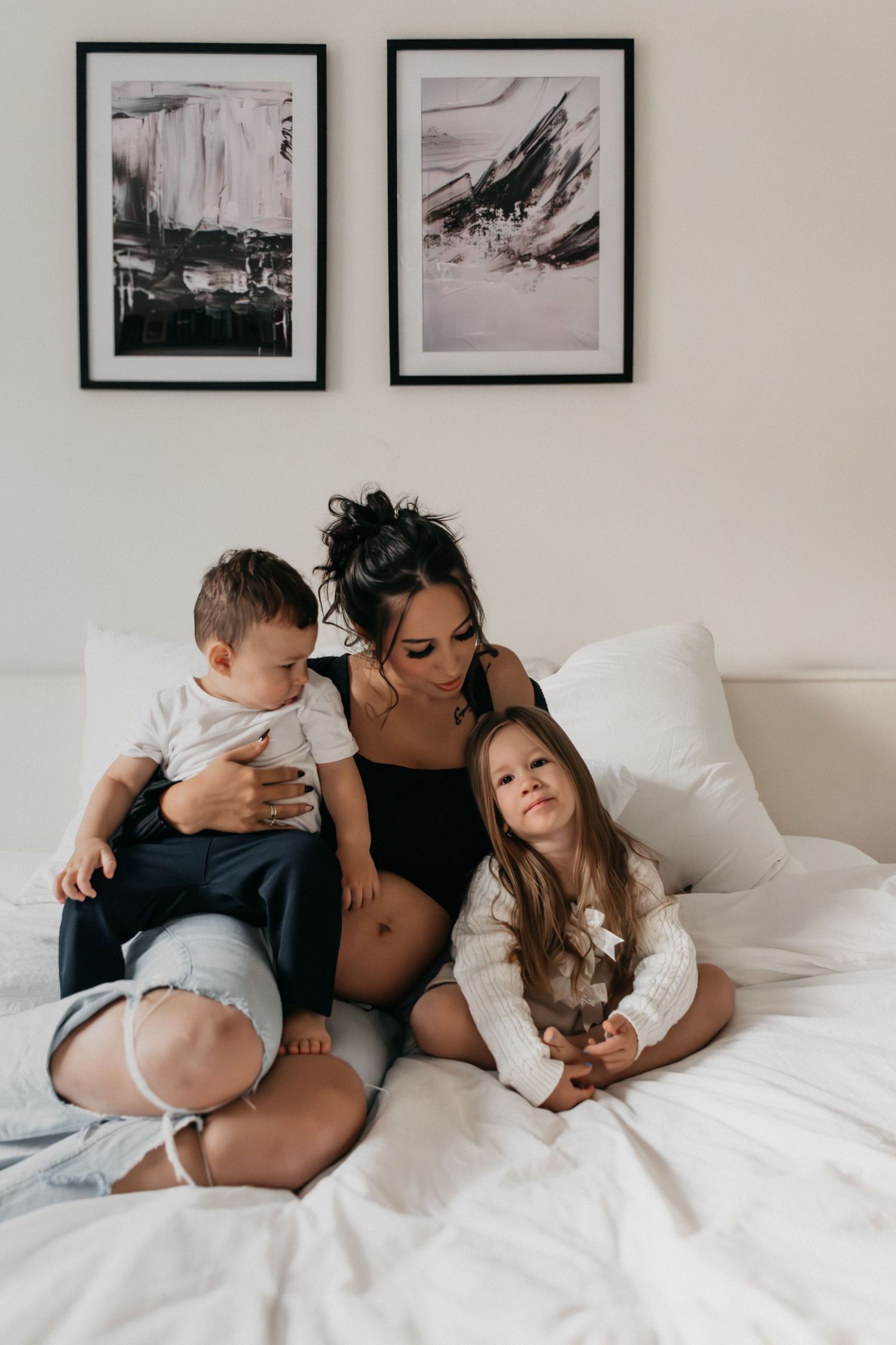 Zärtliche Familienmomente, festgehalten auf weißem Bett mit schwarz-weißen Kunstwerken an der Wand.
