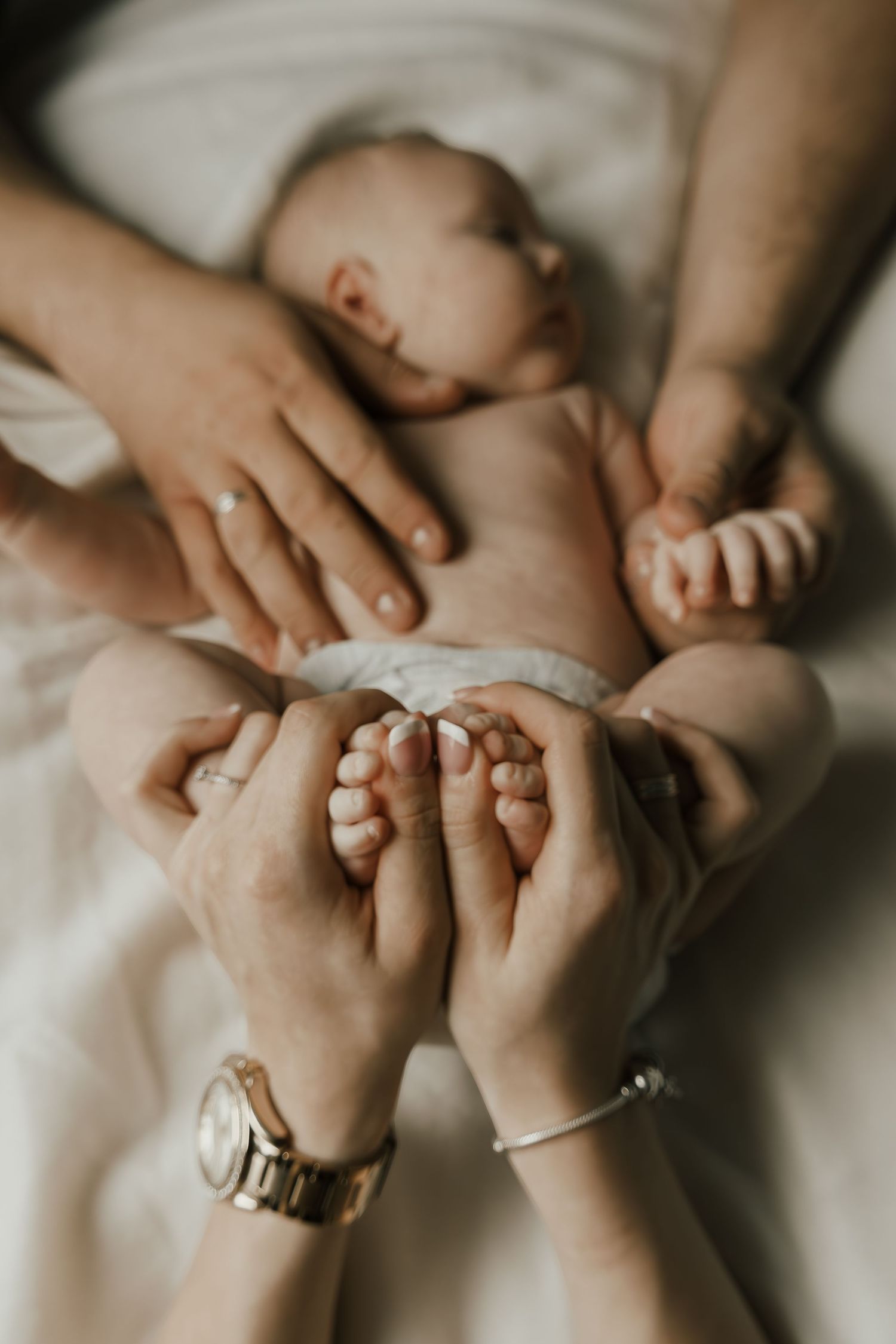 Nahaufnahme von ineinander verschlungenen Händen mit Ringen, die Baby umarmen