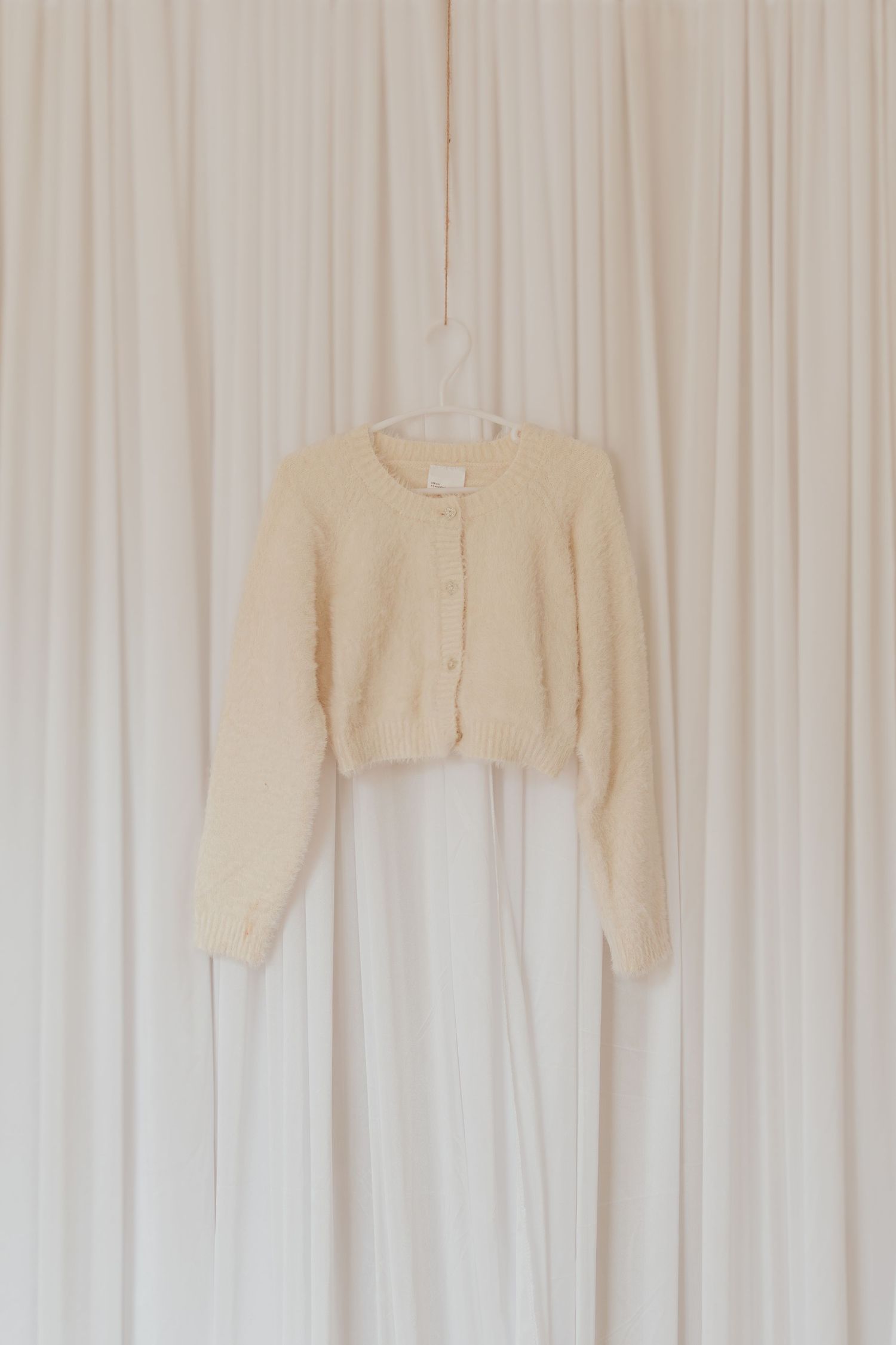 Beige oder cremefarbene Pullover, die an weißen Vorhängen an einer Wand hängen.