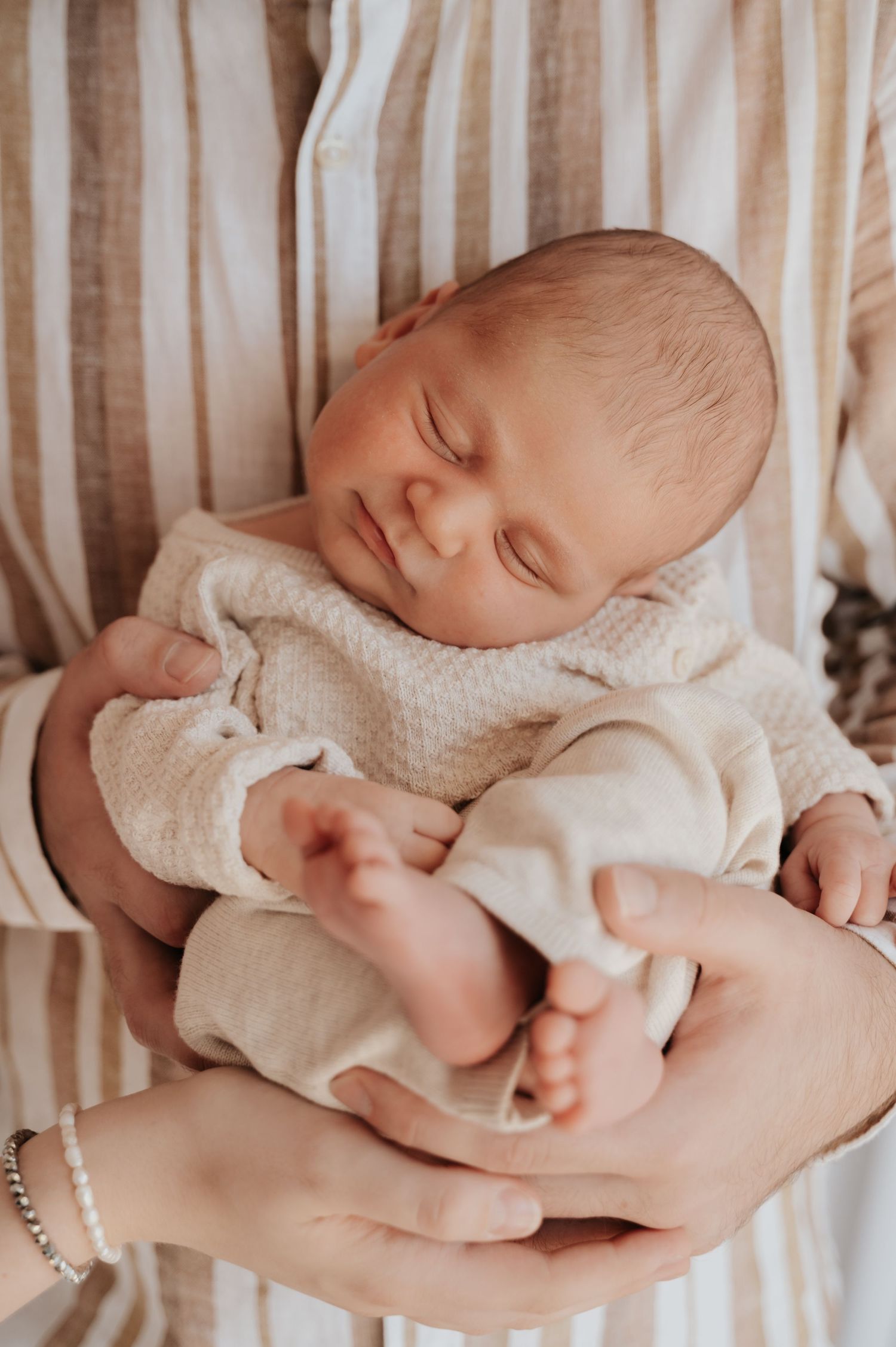 A peaceful newborn baby sleeping in an adult's hands, wearing a cream waffle knit outfit.